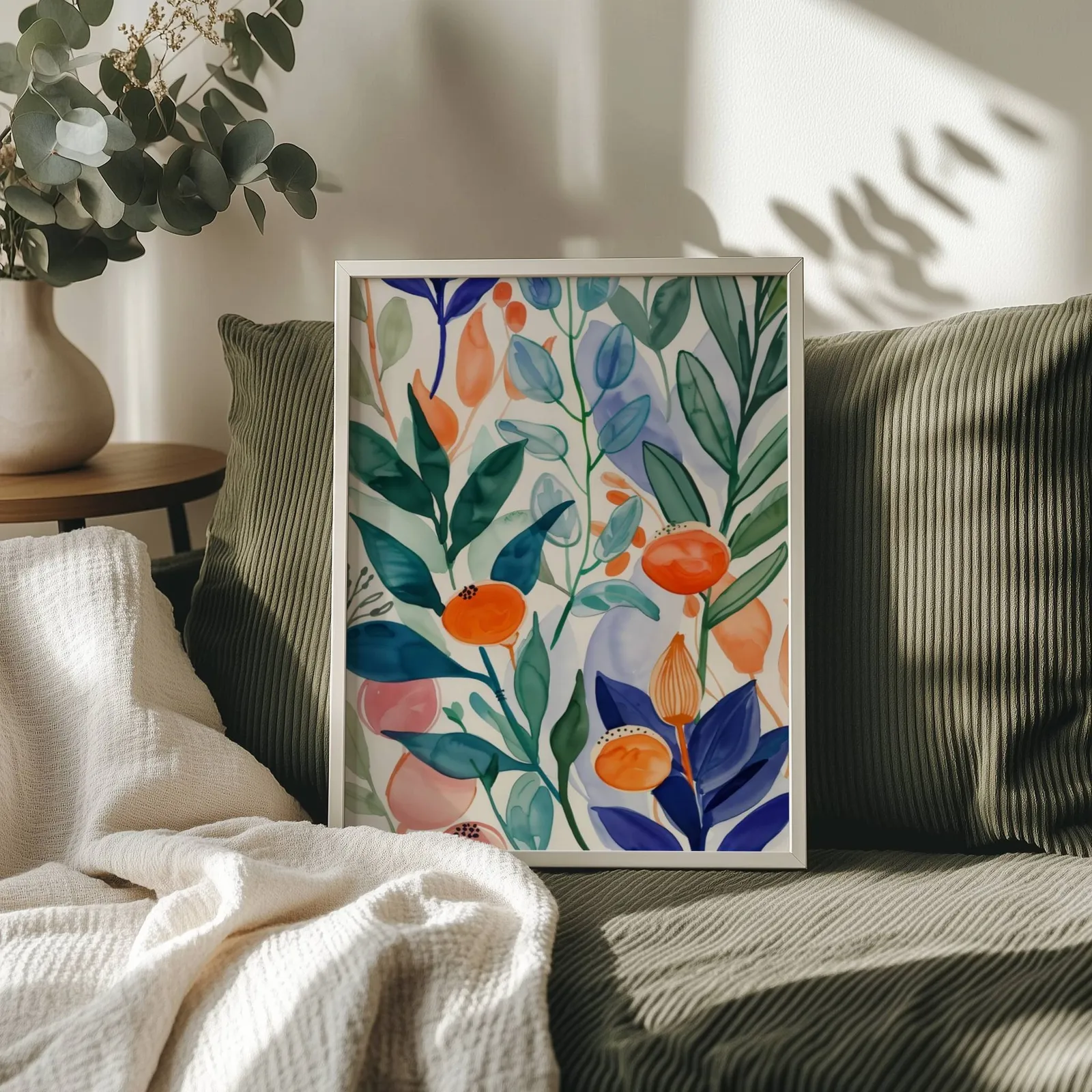 colorful botanical floral wall art, propped on an olive corduroy sofa beside a eucalyptus vase