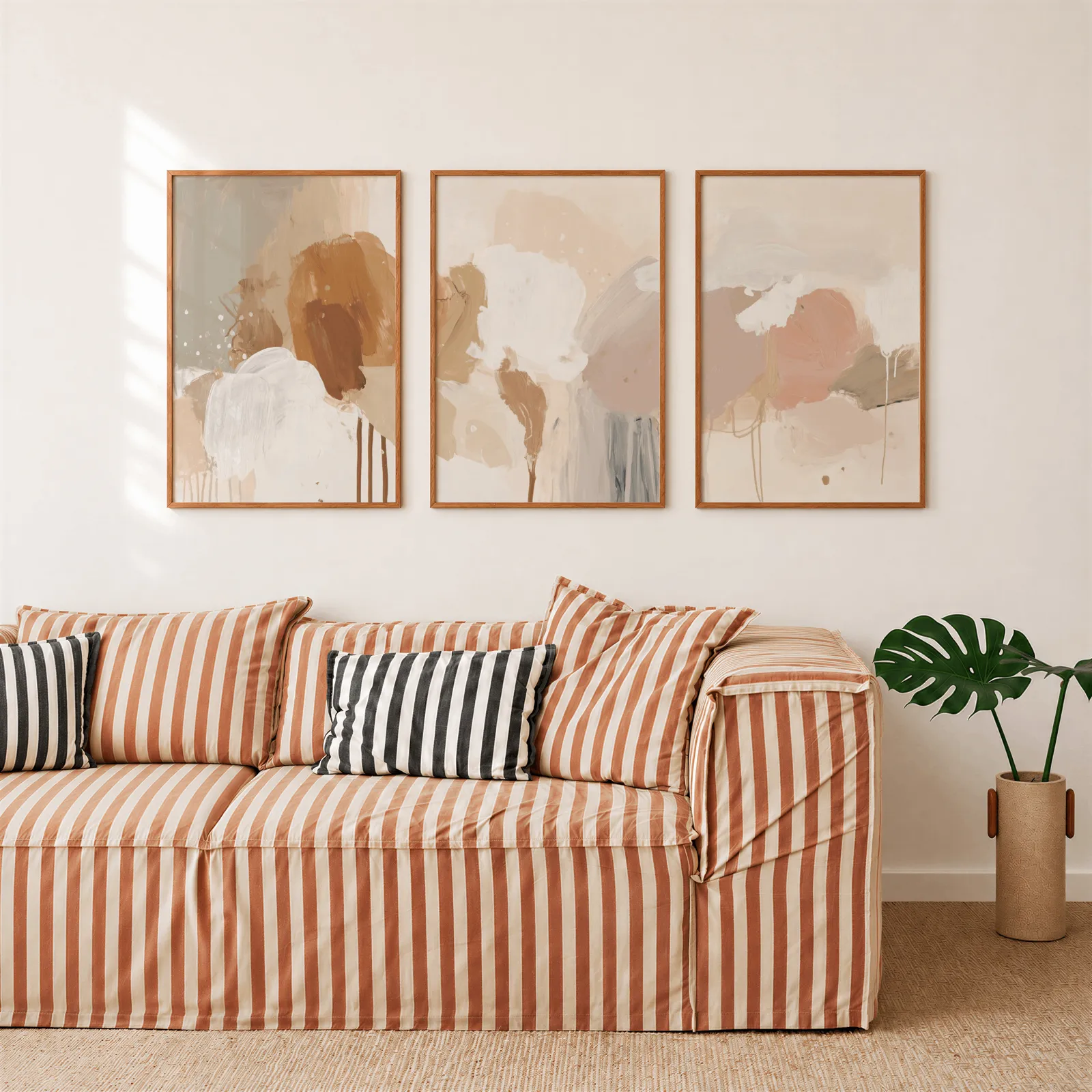 terracotta abstract wall art set of 3, above a rust-striped sofa beside a potted monstera