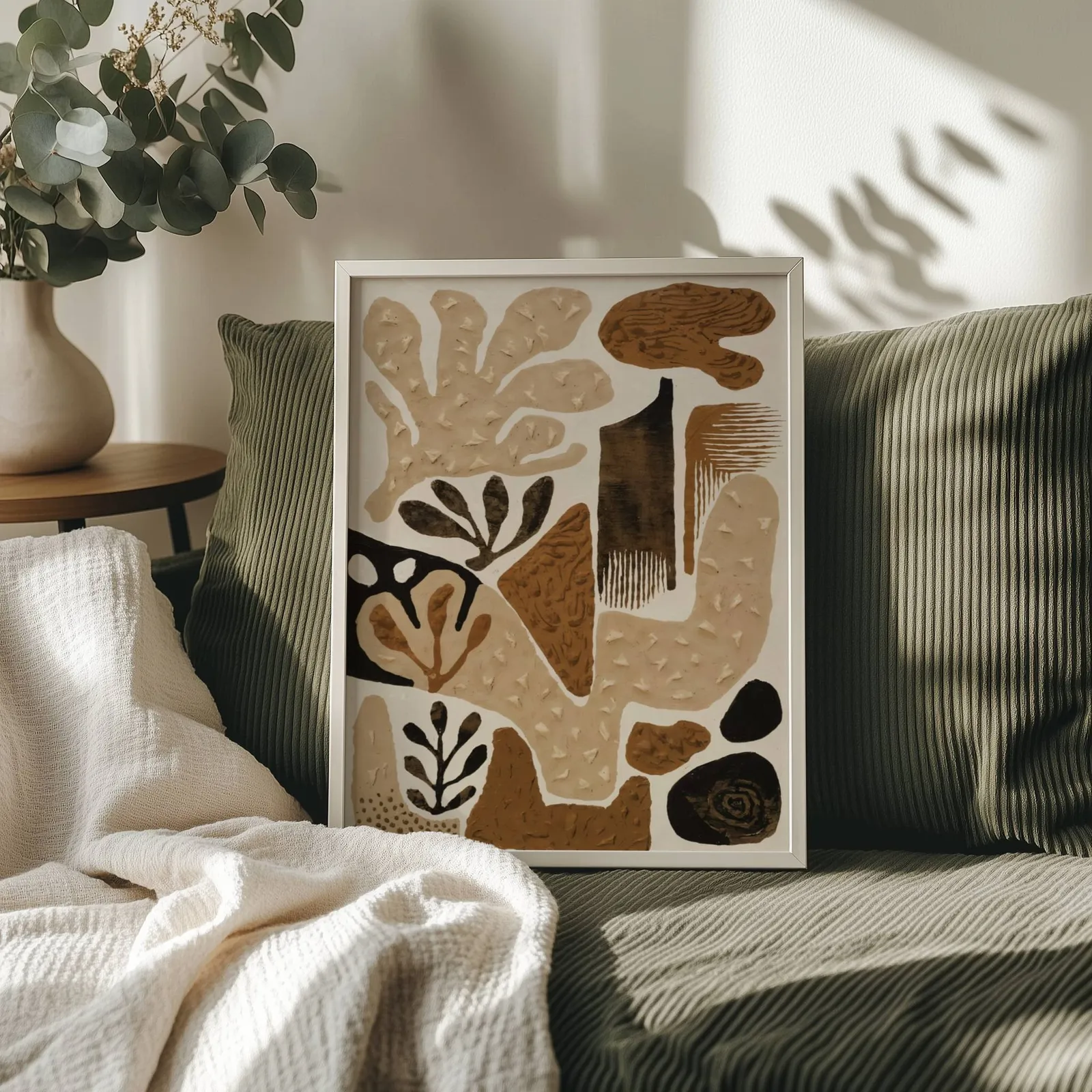 brown abstract botanical wall art, propped on an olive corduroy sofa beside a eucalyptus vase