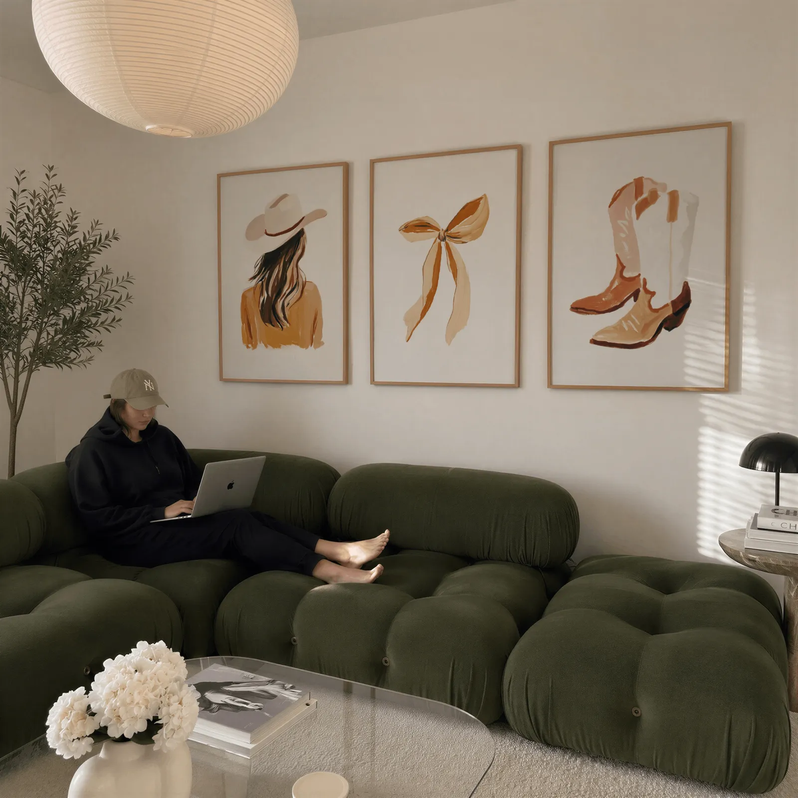 western cowgirl wall art set of three terracotta prints, above a plush olive velvet sectional beneath a paper lantern light