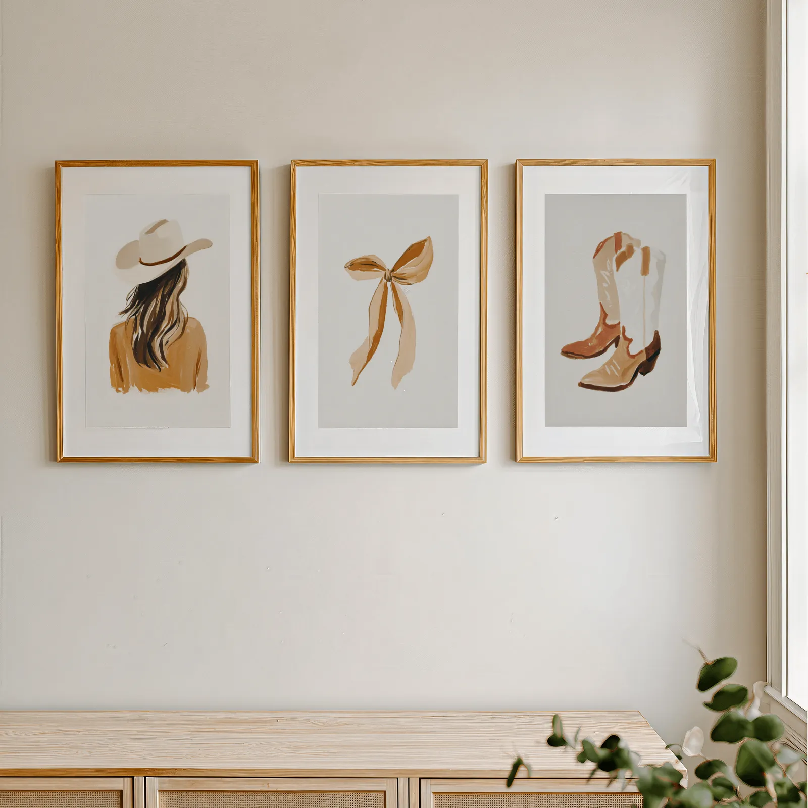 western cowgirl wall art set of three terracotta prints, in a row above a light wooden sideboard near a window