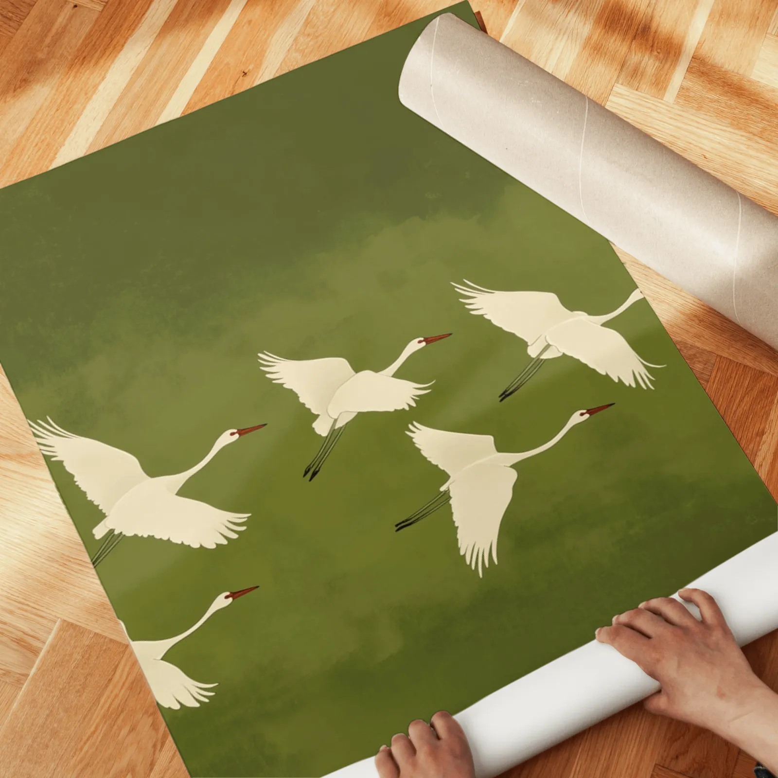 green crane wall art set of 3, unrolled across a herringbone wood floor by hand