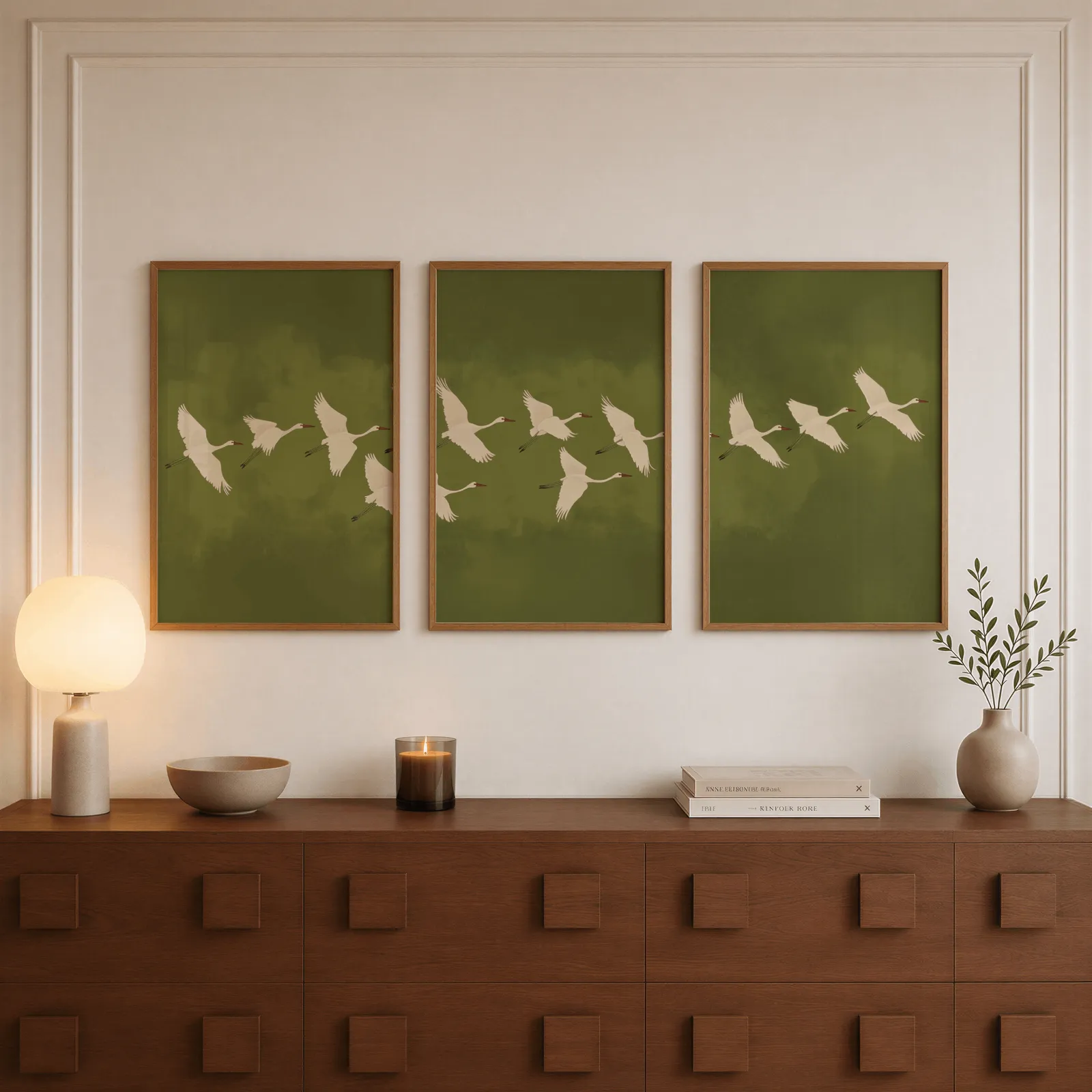 green crane wall art set of 3, above a walnut sideboard with a lit candle and glowing lamp