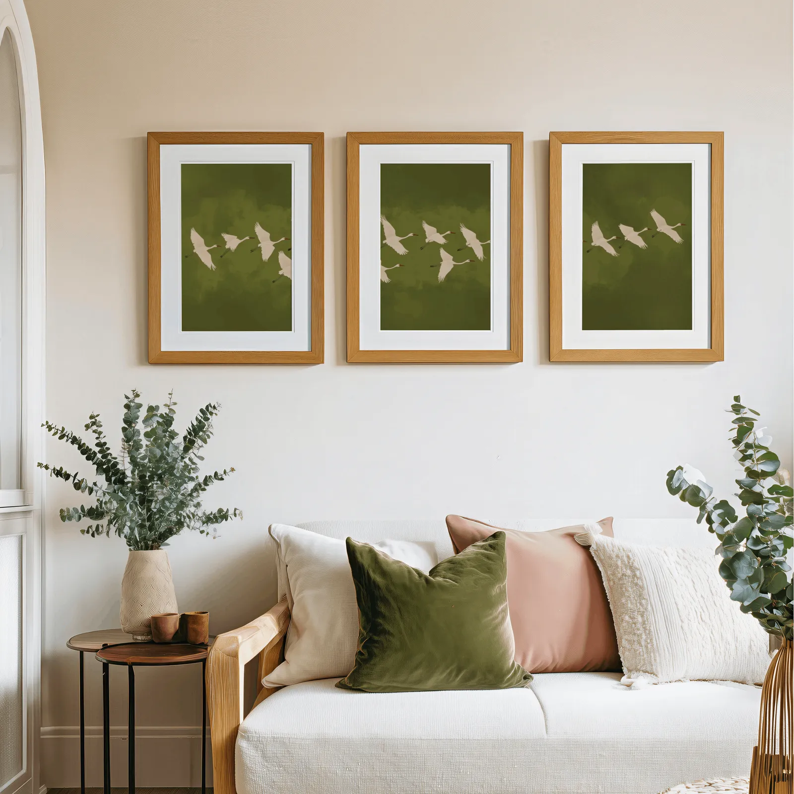 green crane wall art set of 3, above a cream sofa piled with olive and blush pillows
