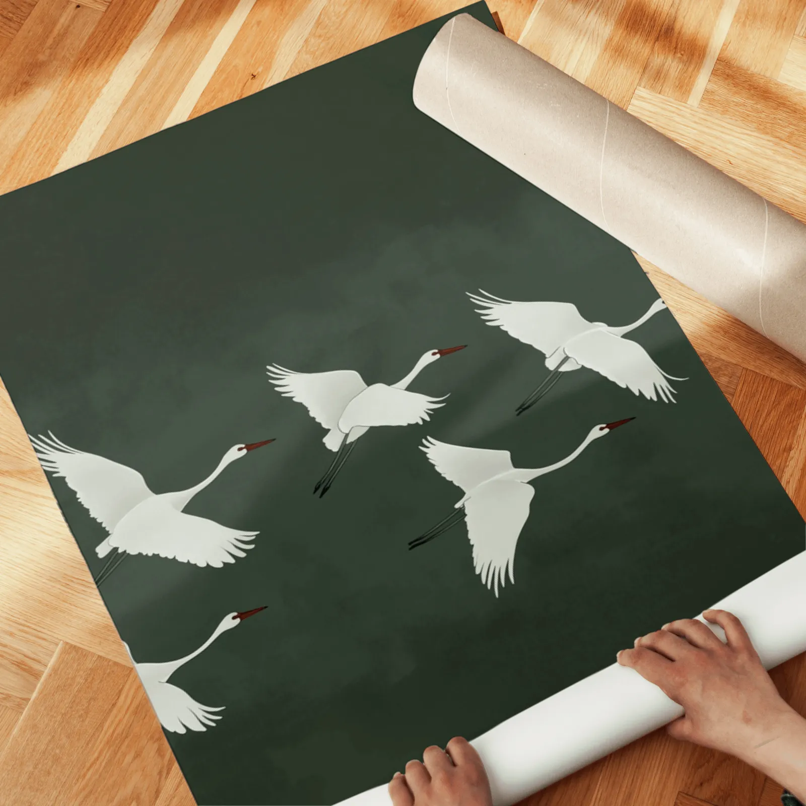 green crane wall art set of 3, unrolled across a herringbone wood floor by hand