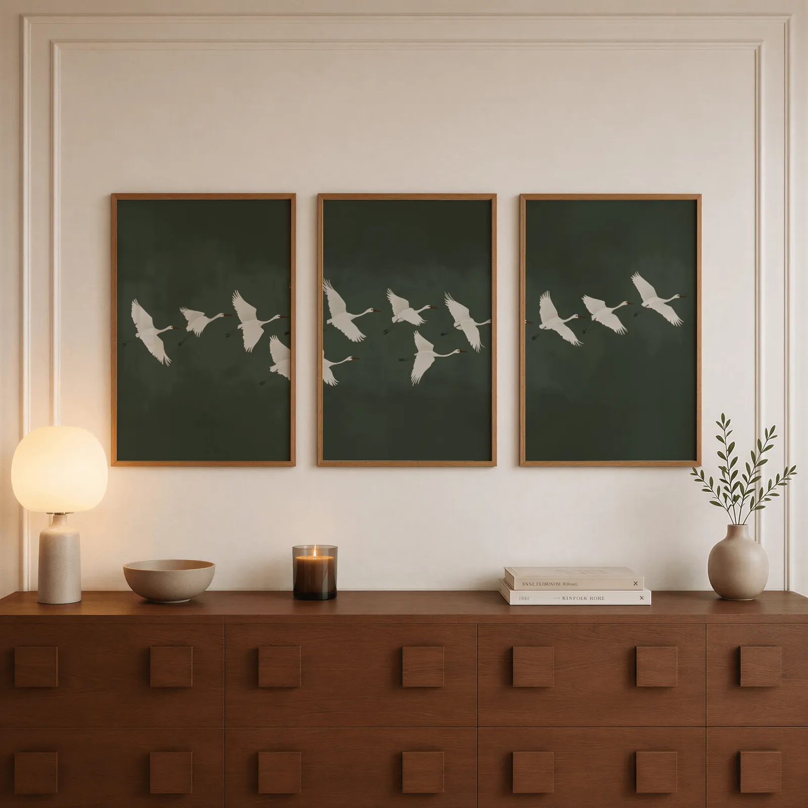 green crane wall art set of 3, above a walnut sideboard with a lit candle and glowing lamp