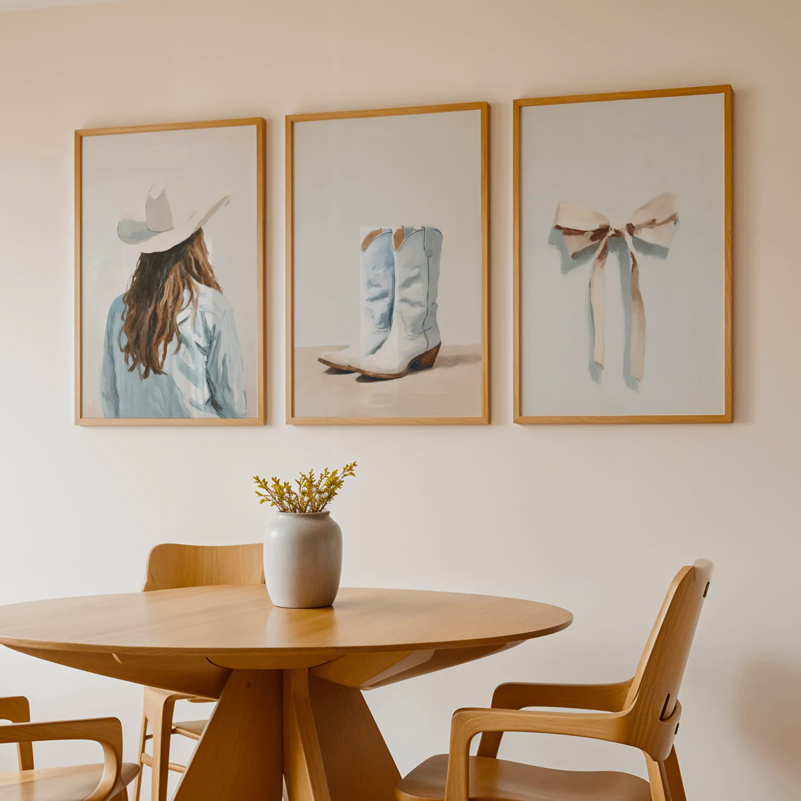 western cowgirl wall art set with boots and bow, above a round wooden table with a stoneware vase