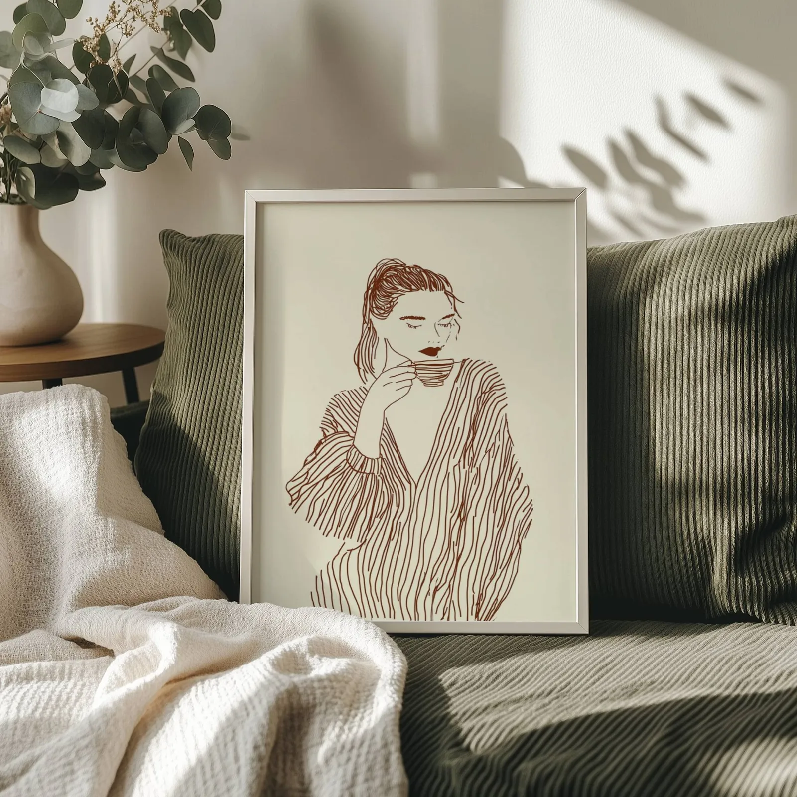 woman drinking coffee line art print, propped on an olive corduroy sofa beside a eucalyptus vase