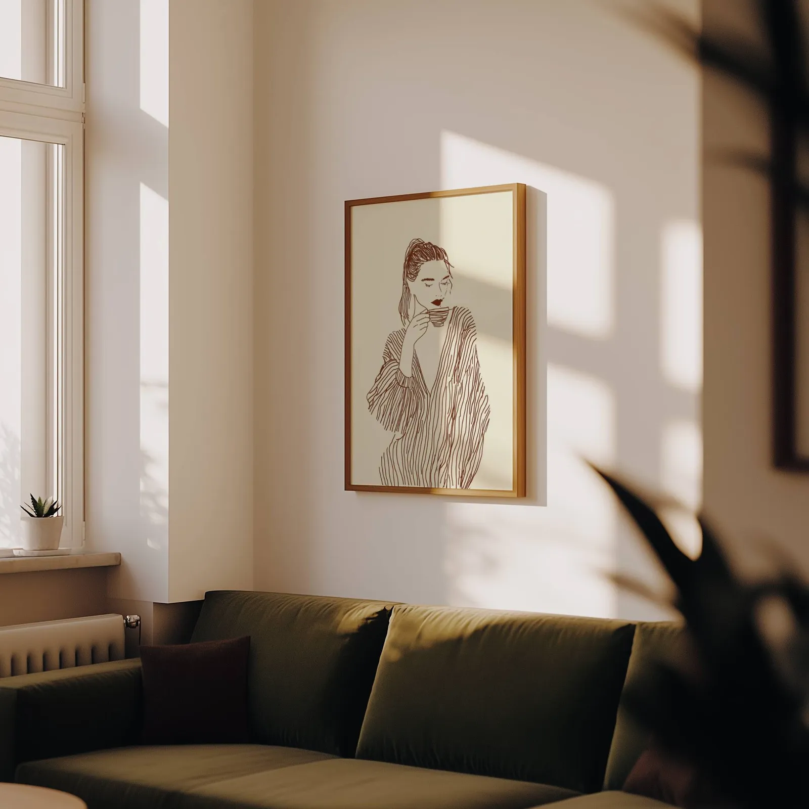 woman drinking coffee line art print, above an olive velvet sofa in raking afternoon light