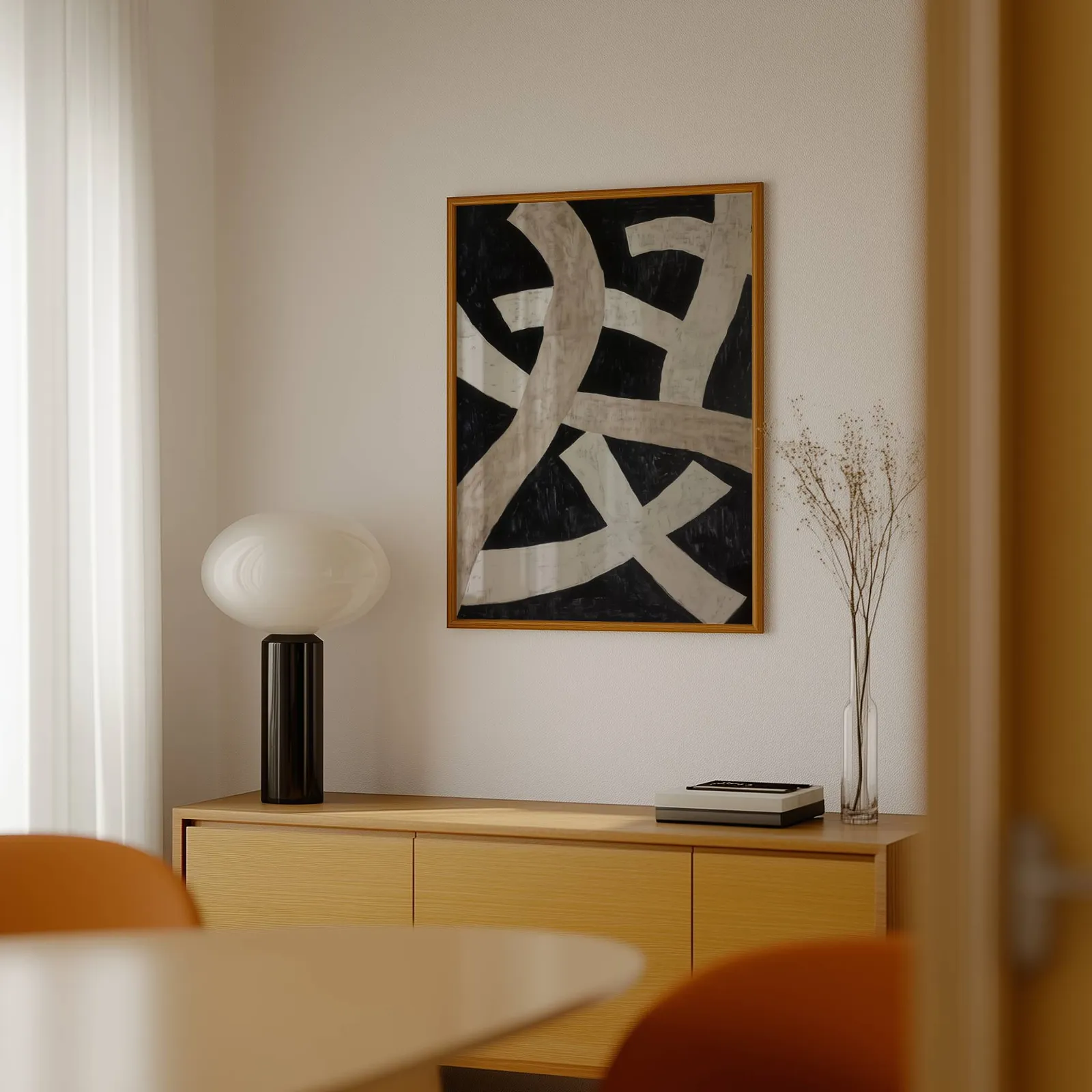 black minimalist abstract wall art with cream ribbons, above a light wood sideboard beside a bulbous black lamp