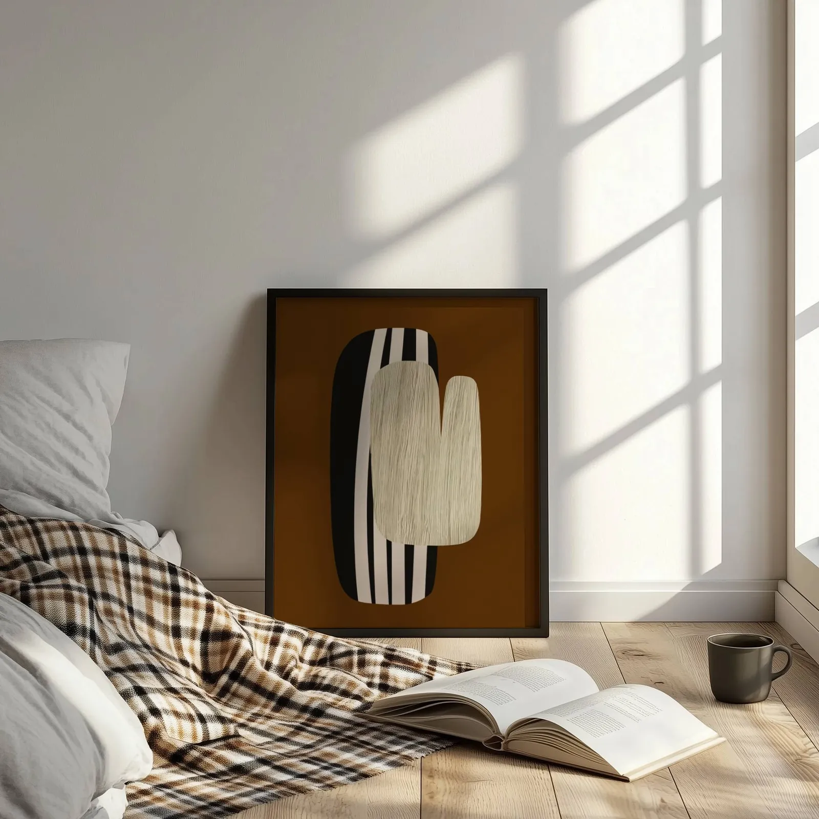 brown abstract wall art, leaning on the floor beside a plaid throw and open book