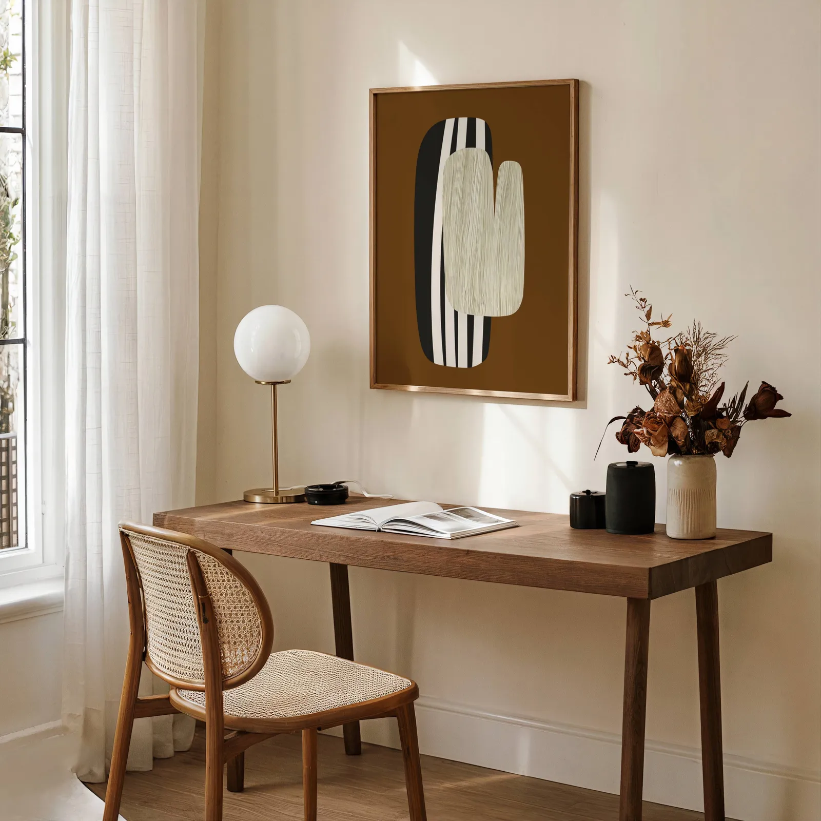 brown abstract wall art, above a wooden desk with a globe lamp and dried flowers
