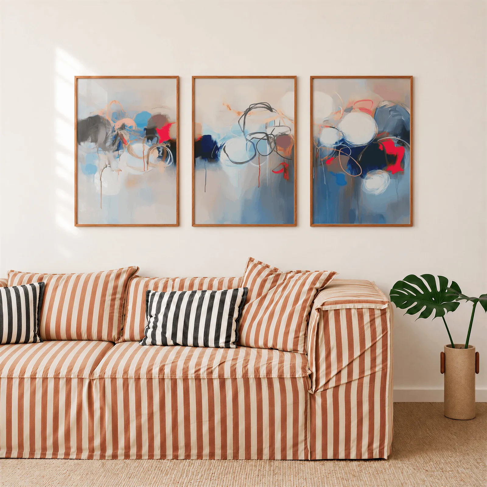 blue red abstract triptych wall art, above a rust-striped sofa beside a potted monstera