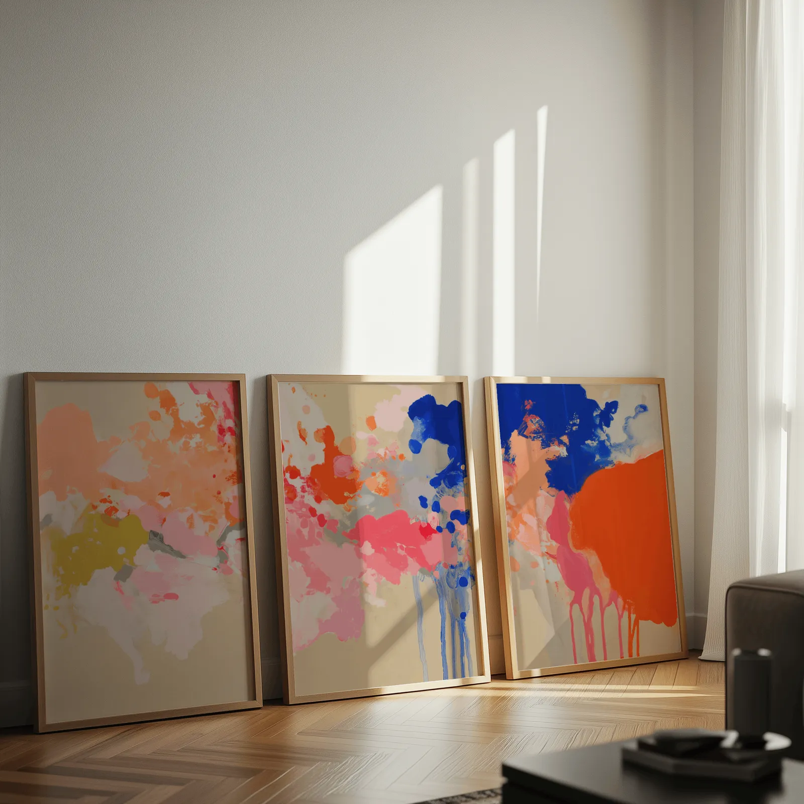 colorful abstract wall art set of three, leaning against a sunlit wall on herringbone flooring