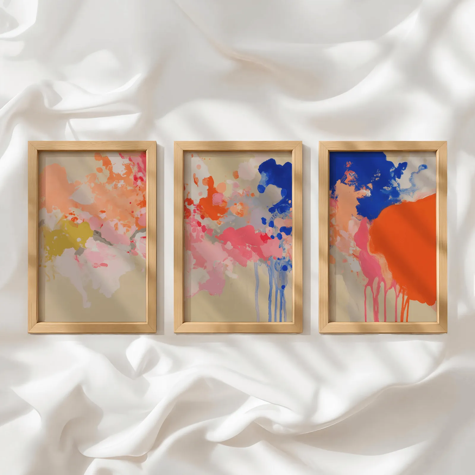 colorful abstract wall art set of three, in a row atop rumpled white silky fabric
