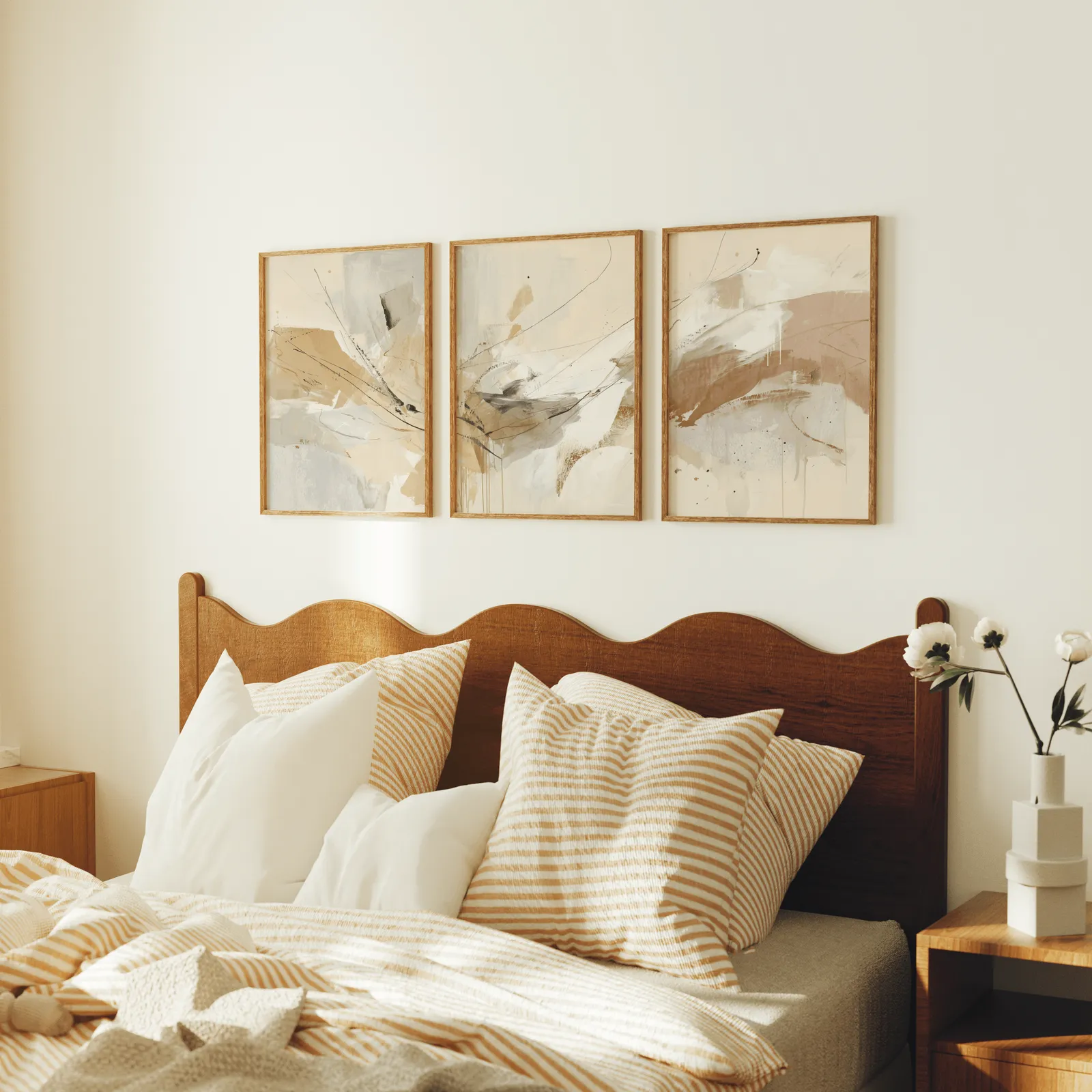 neutral abstract wall art set of 3, above a scalloped wooden headboard with striped pillows