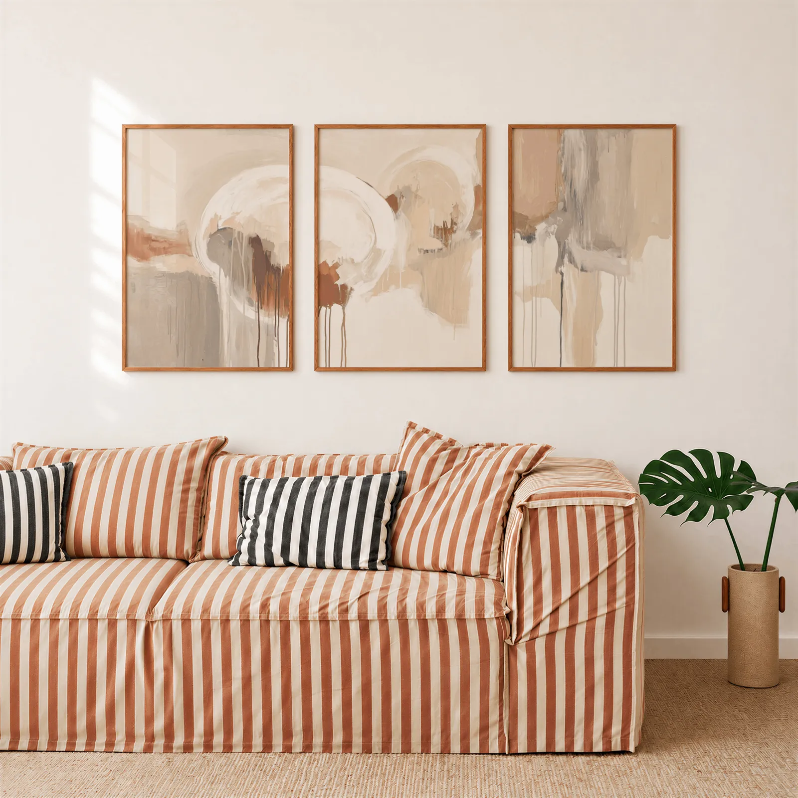 terracotta and grey abstract wall art set of 3, above a rust-striped sofa beside a potted monstera