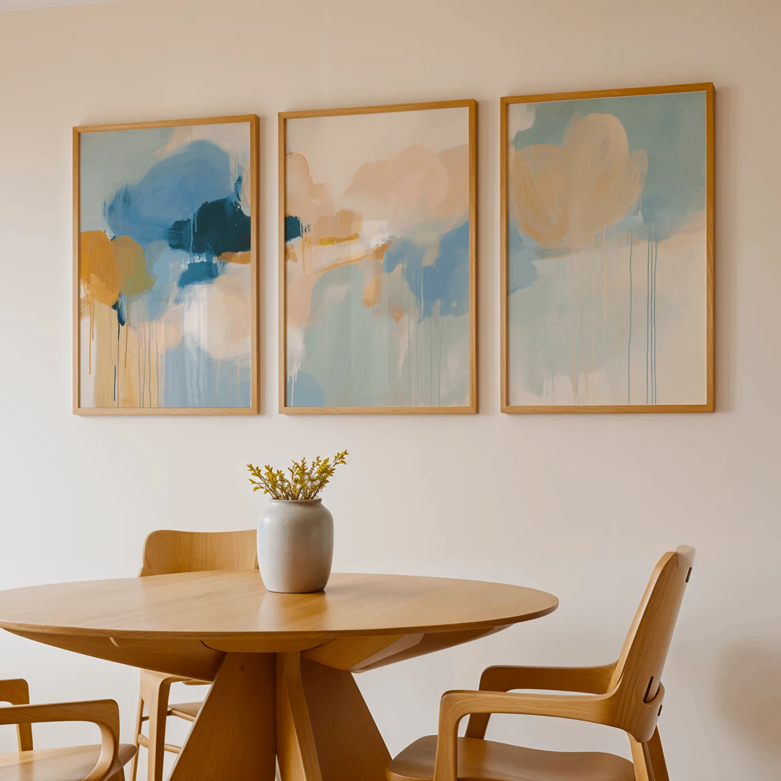 colorful abstract wall art set of 3 in blue and orange, above a round wooden table with a stoneware vase