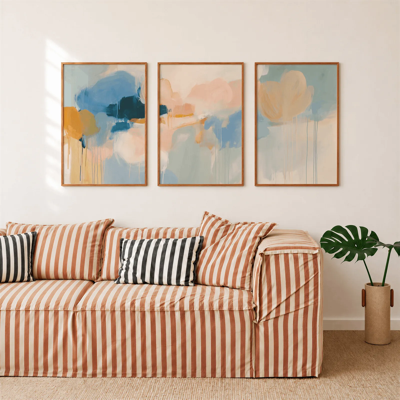 colorful abstract wall art set of 3 in blue and orange, above a rust-striped sofa beside a potted monstera