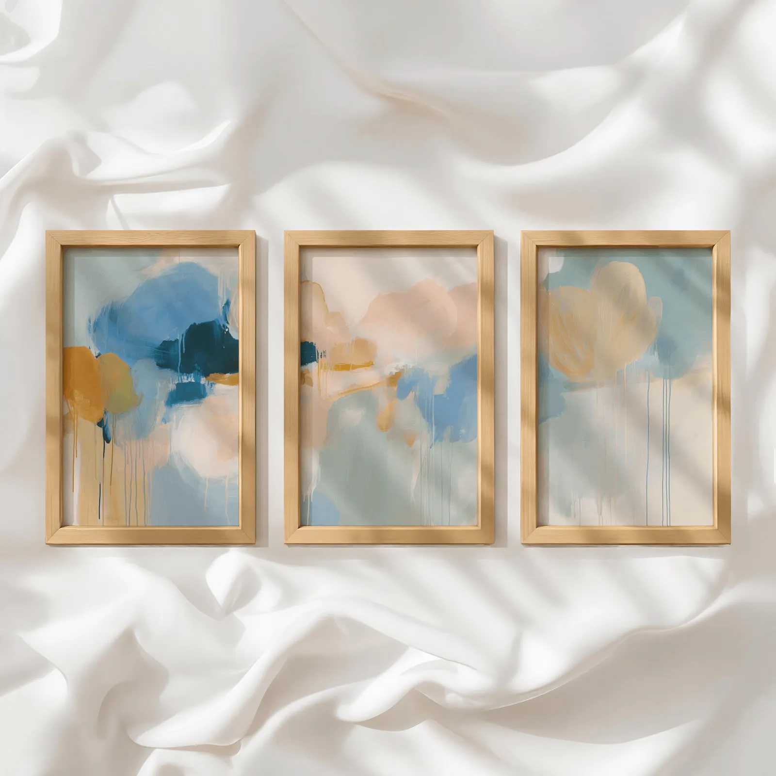 colorful abstract wall art set of 3 in blue and orange, in a row atop rumpled white silky fabric