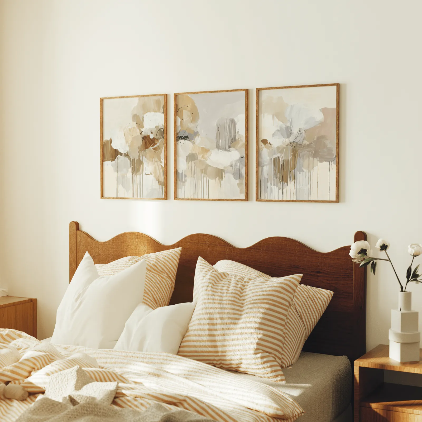beige and grey abstract triptych wall art, above a scalloped wooden headboard with striped pillows