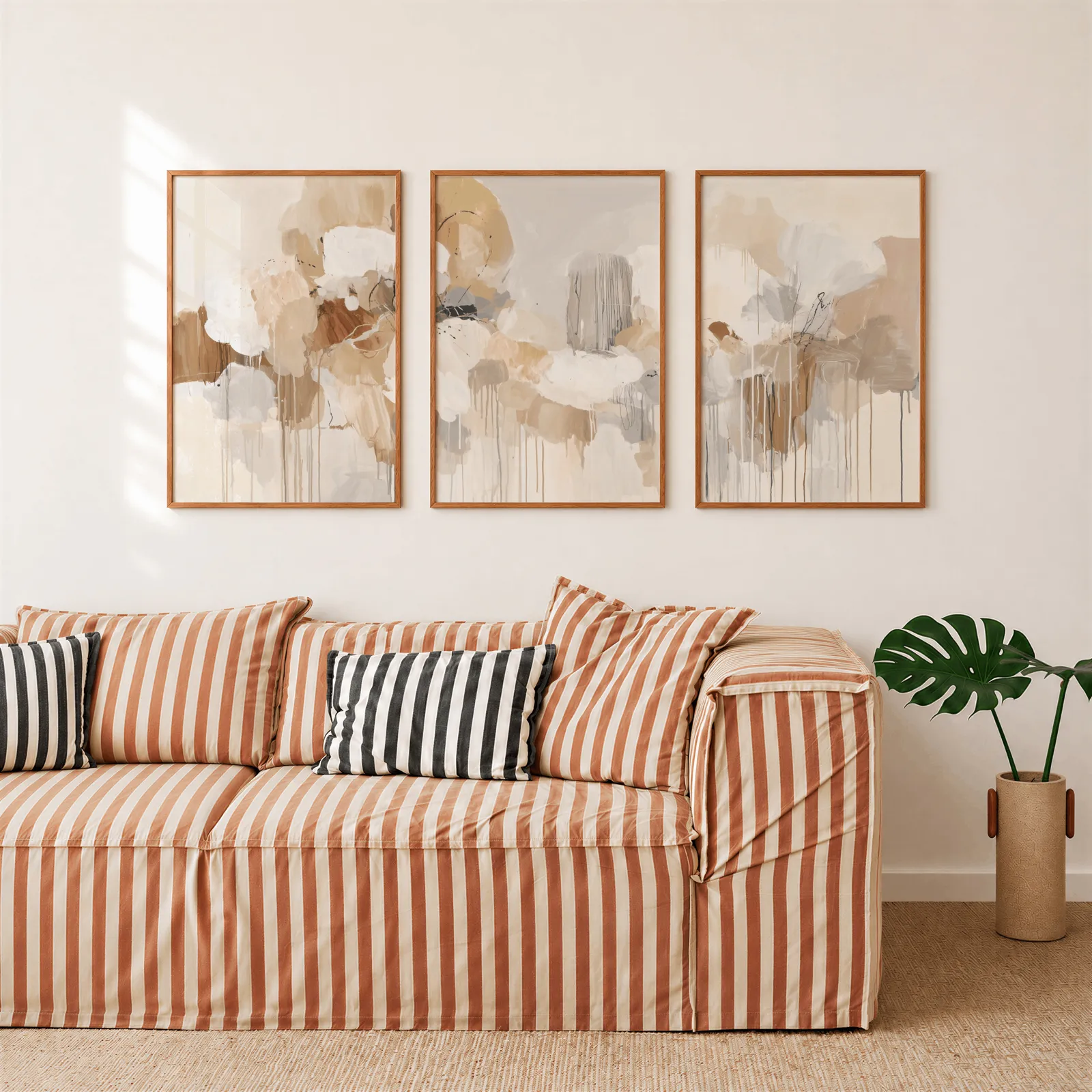 beige and grey abstract triptych wall art, above a rust-striped sofa beside a potted monstera