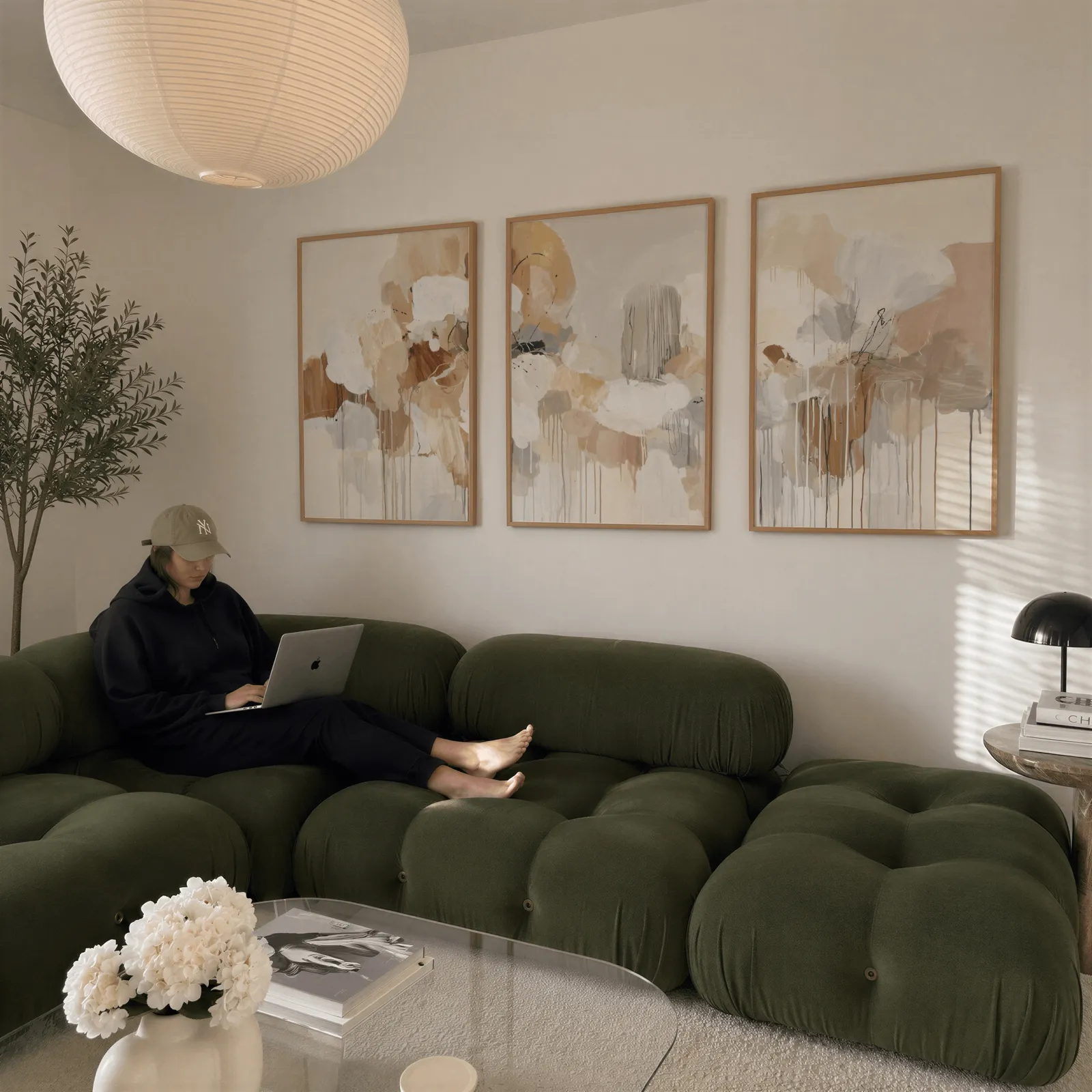beige and grey abstract triptych wall art, above a plush olive velvet sectional beneath a paper lantern light