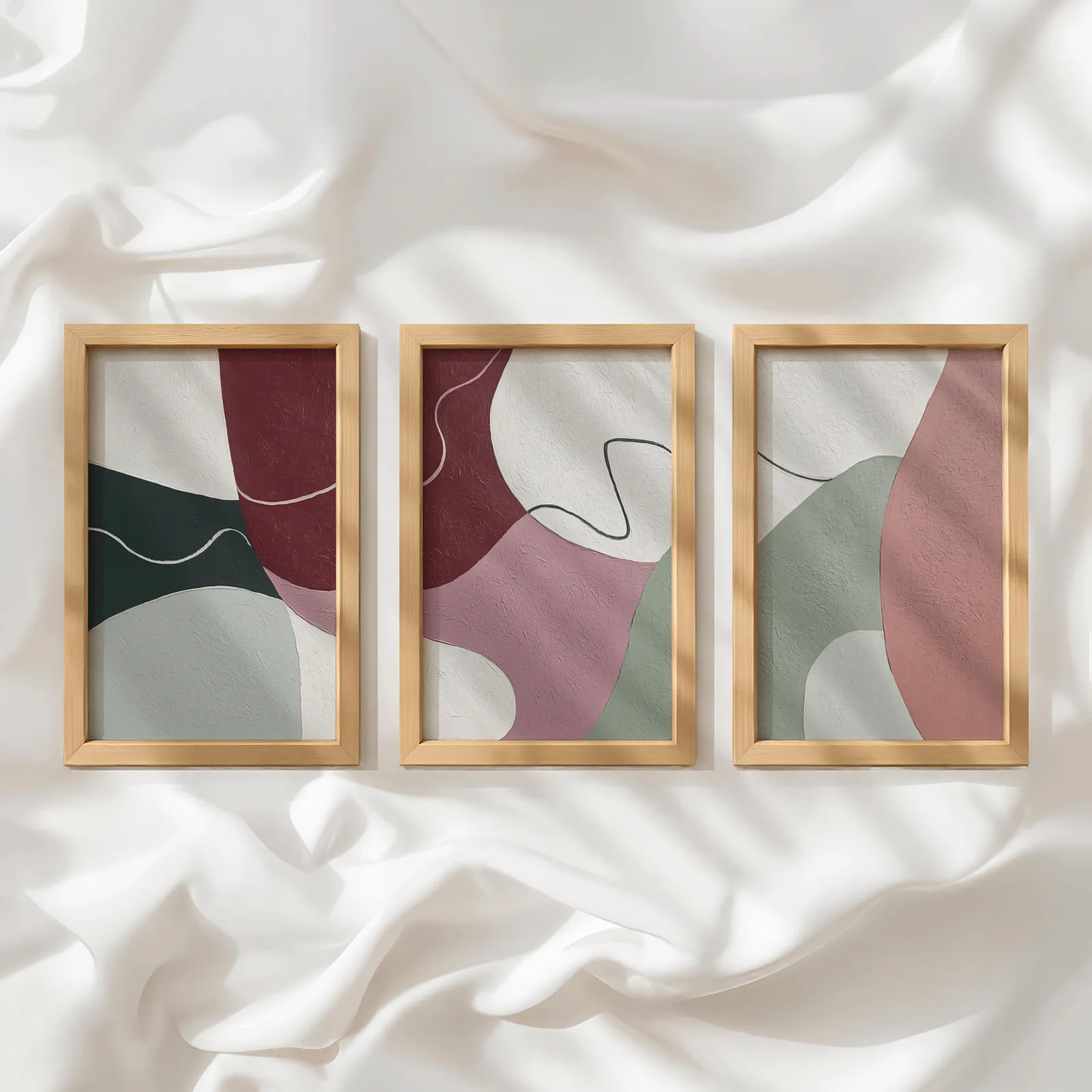 abstract triptych wall art in burgundy and pink, in a row atop rumpled white silky fabric