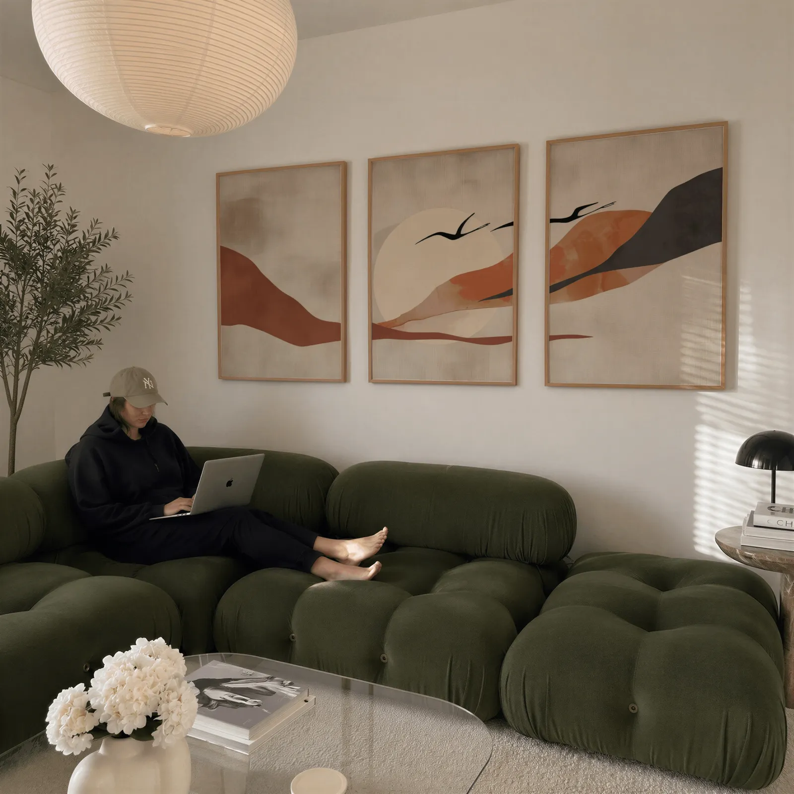 terracotta landscape wall art set of 3 with birds, above a plush olive velvet sectional beneath a paper lantern light
