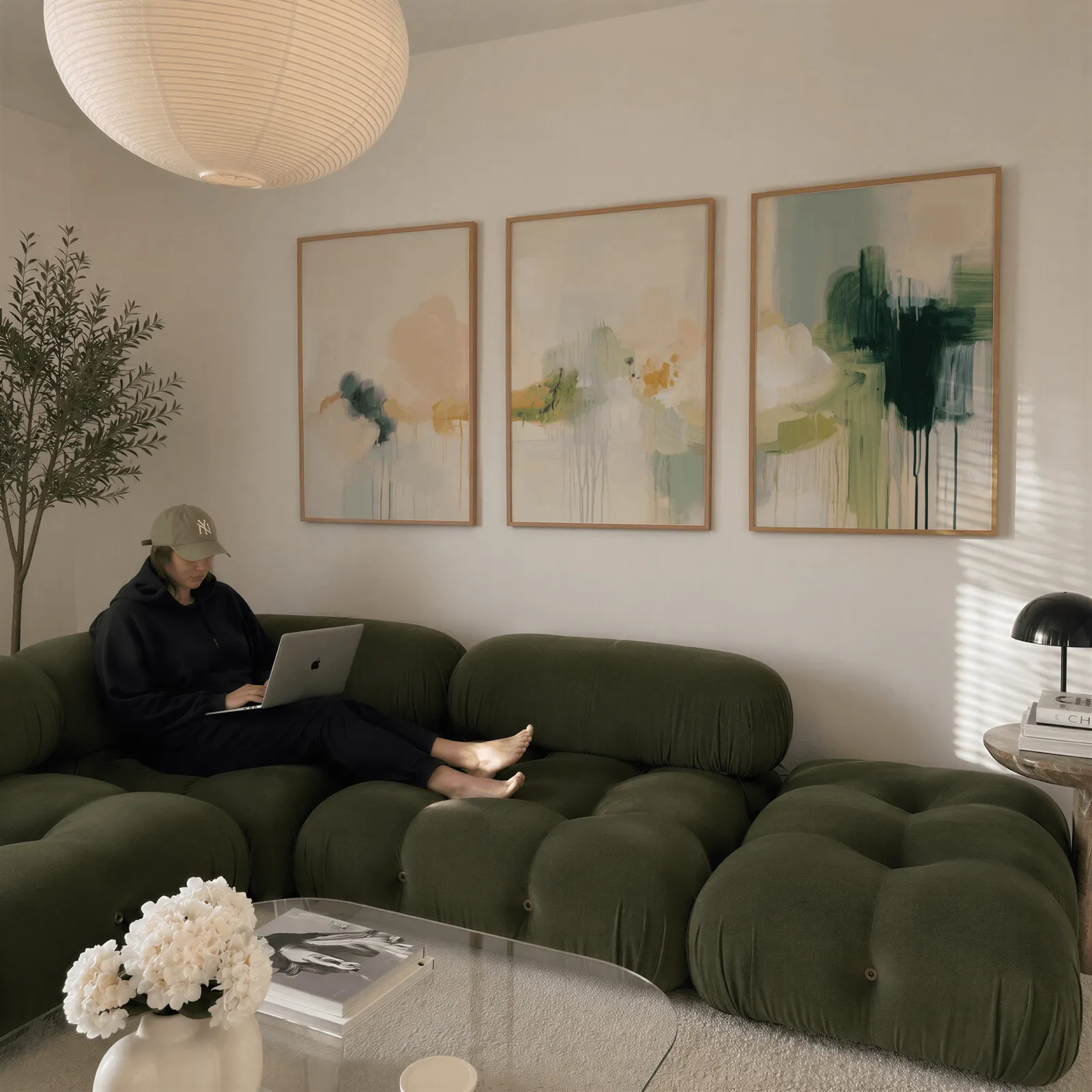 abstract wall art triptych in green and terracotta, above a plush olive velvet sectional beneath a paper lantern light