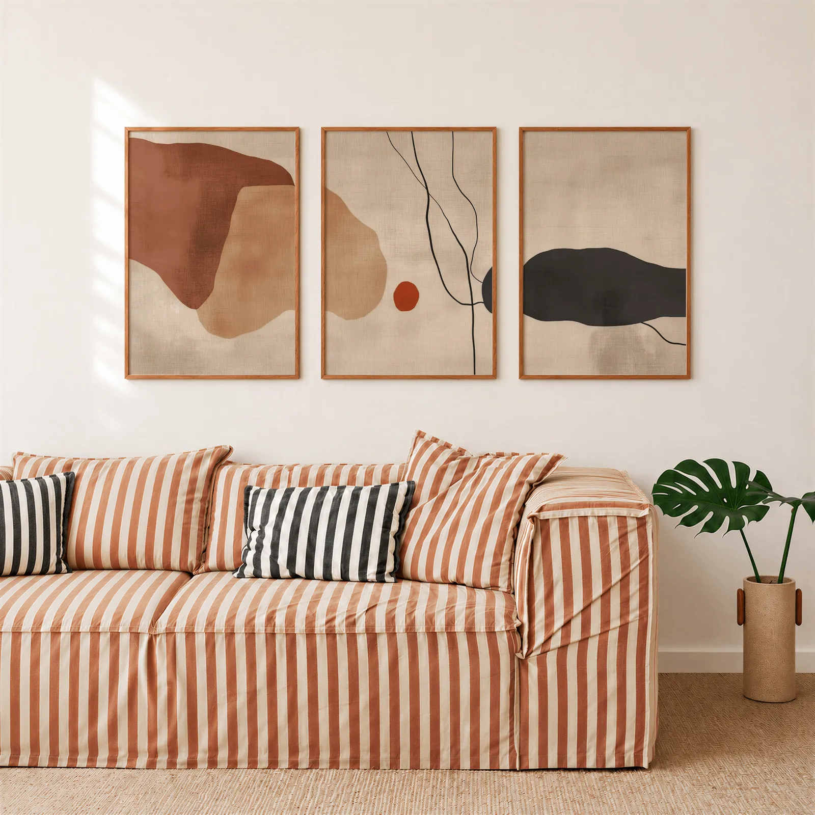 terracotta abstract minimalist wall art set of 3, above a rust-striped sofa beside a potted monstera