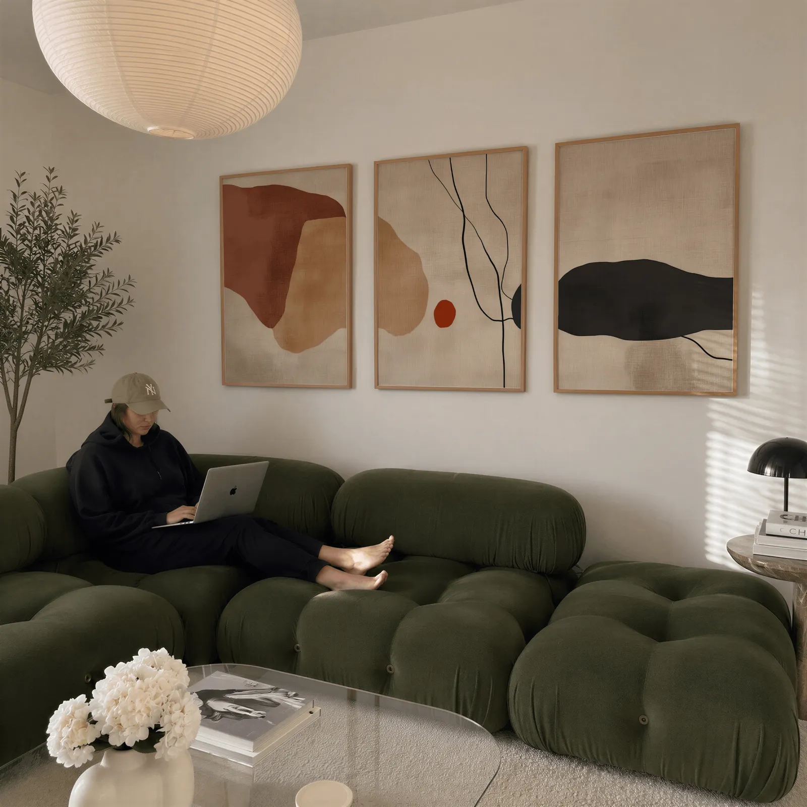 terracotta abstract minimalist wall art set of 3, above a plush olive velvet sectional beneath a paper lantern light