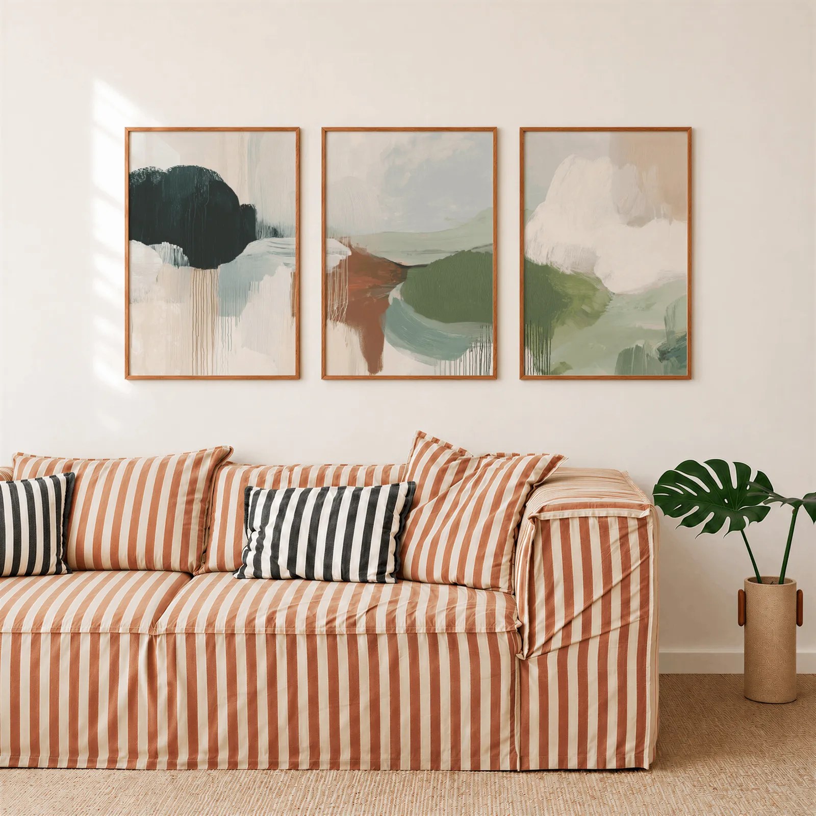 green terracotta abstract wall art set of 3, above a rust-striped sofa beside a potted monstera
