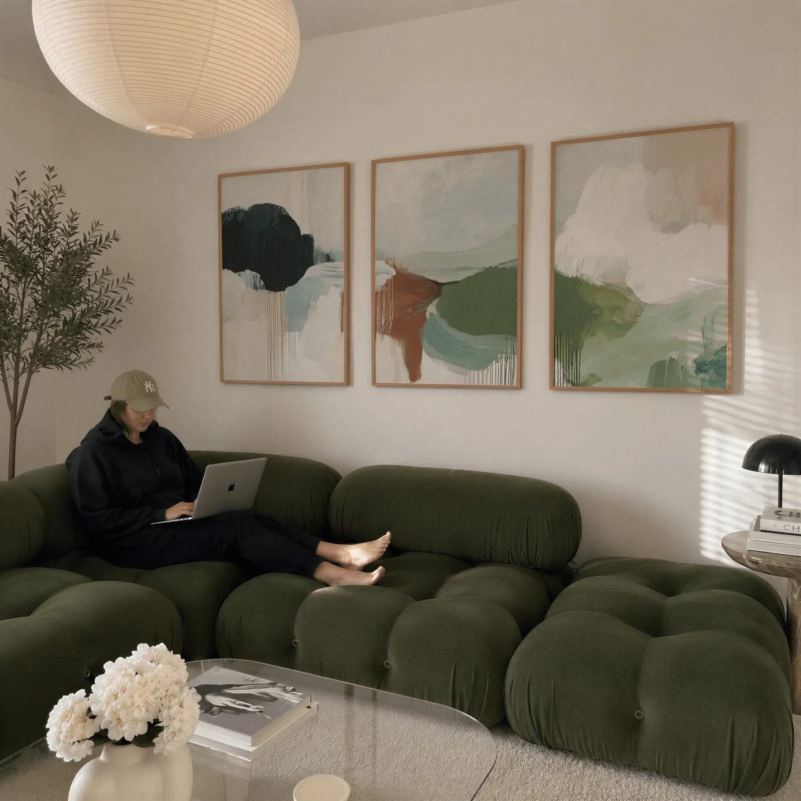 green terracotta abstract wall art set of 3, above a plush olive velvet sectional beneath a paper lantern light