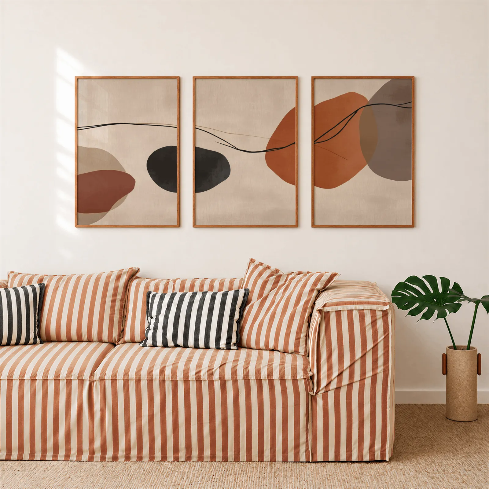 terracotta abstract set of 3 wall art, above a rust-striped sofa beside a potted monstera