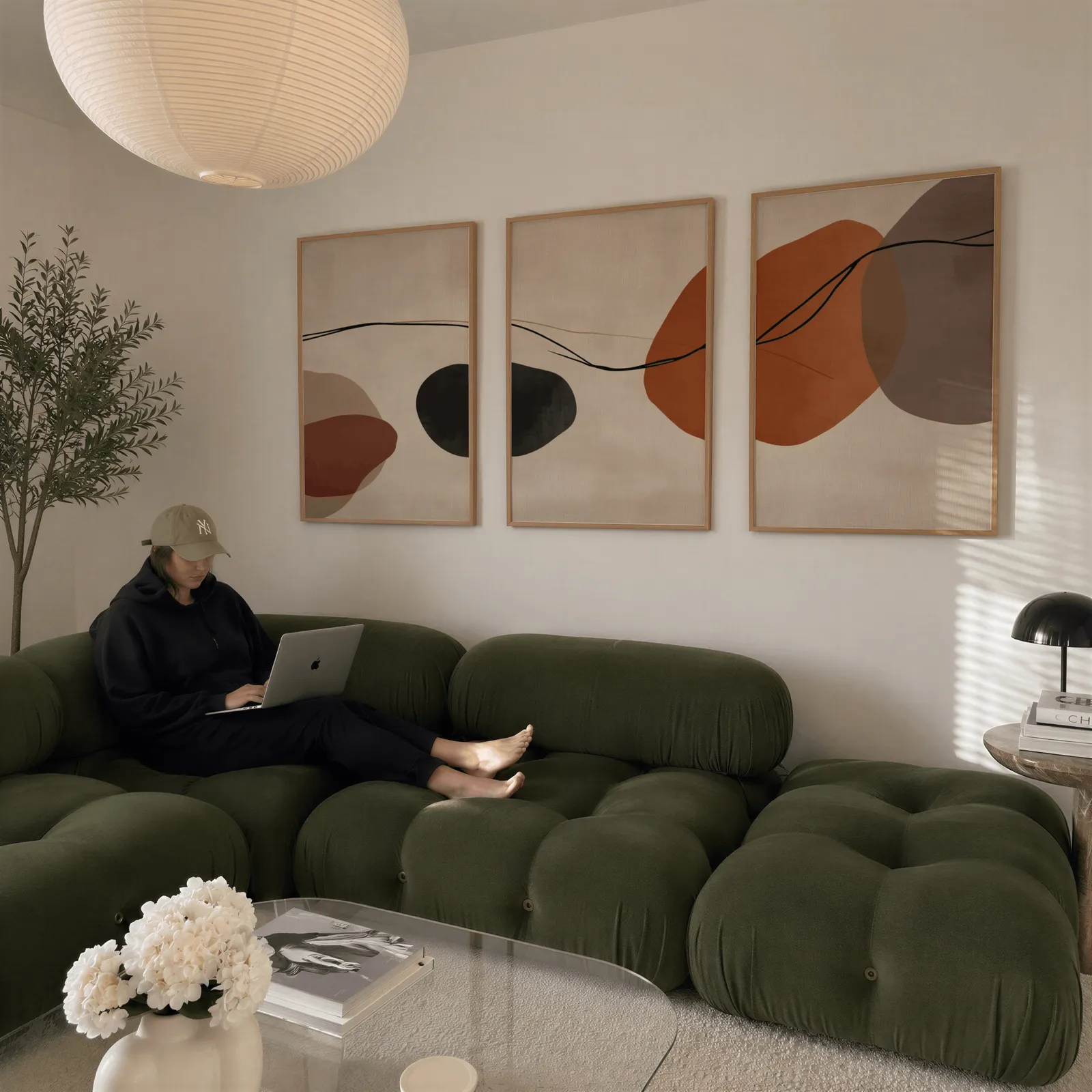 terracotta abstract set of 3 wall art, above a plush olive velvet sectional beneath a paper lantern light