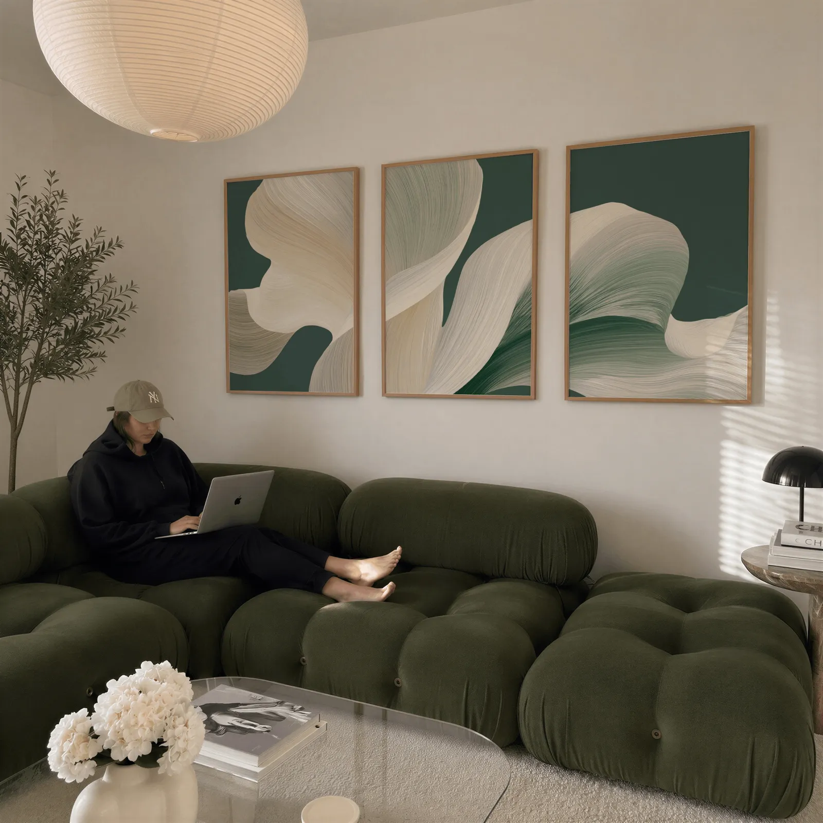 green abstract three piece wall art, above a plush olive velvet sectional beneath a paper lantern light