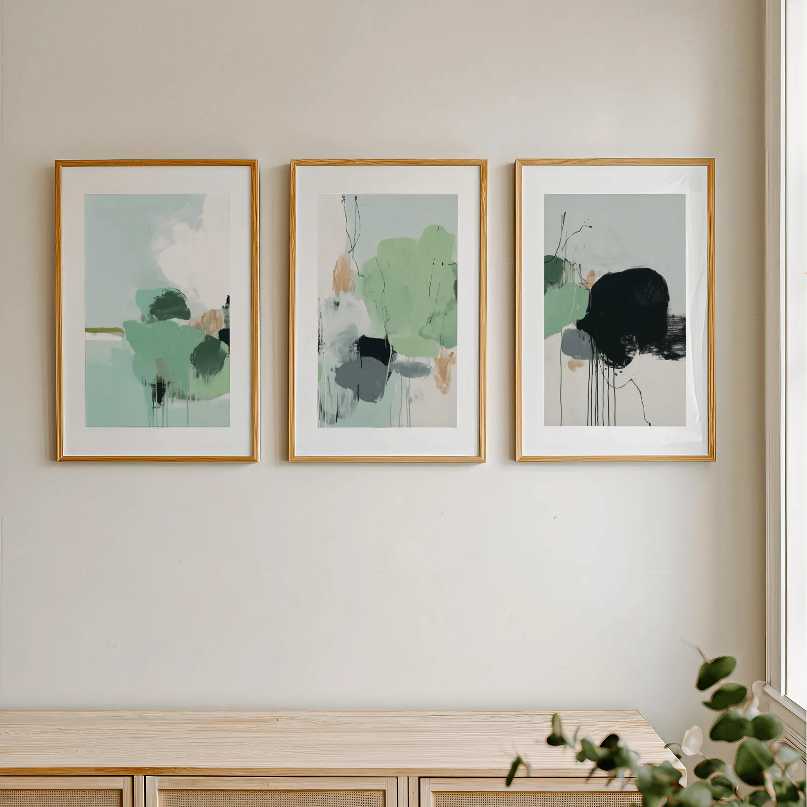 green abstract three piece wall art with black accents, in a row above a light wooden sideboard near a window
