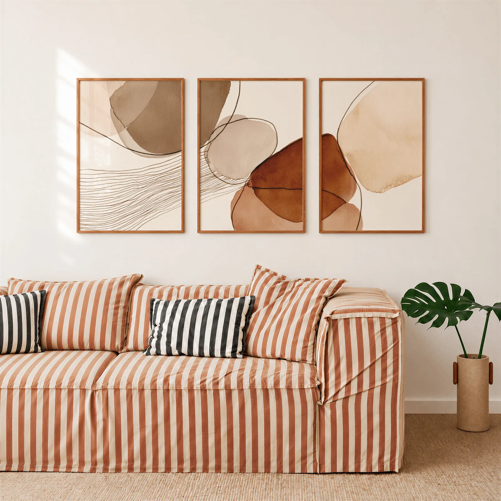 terracotta abstract wall art set of 3, above a rust-striped sofa beside a potted monstera