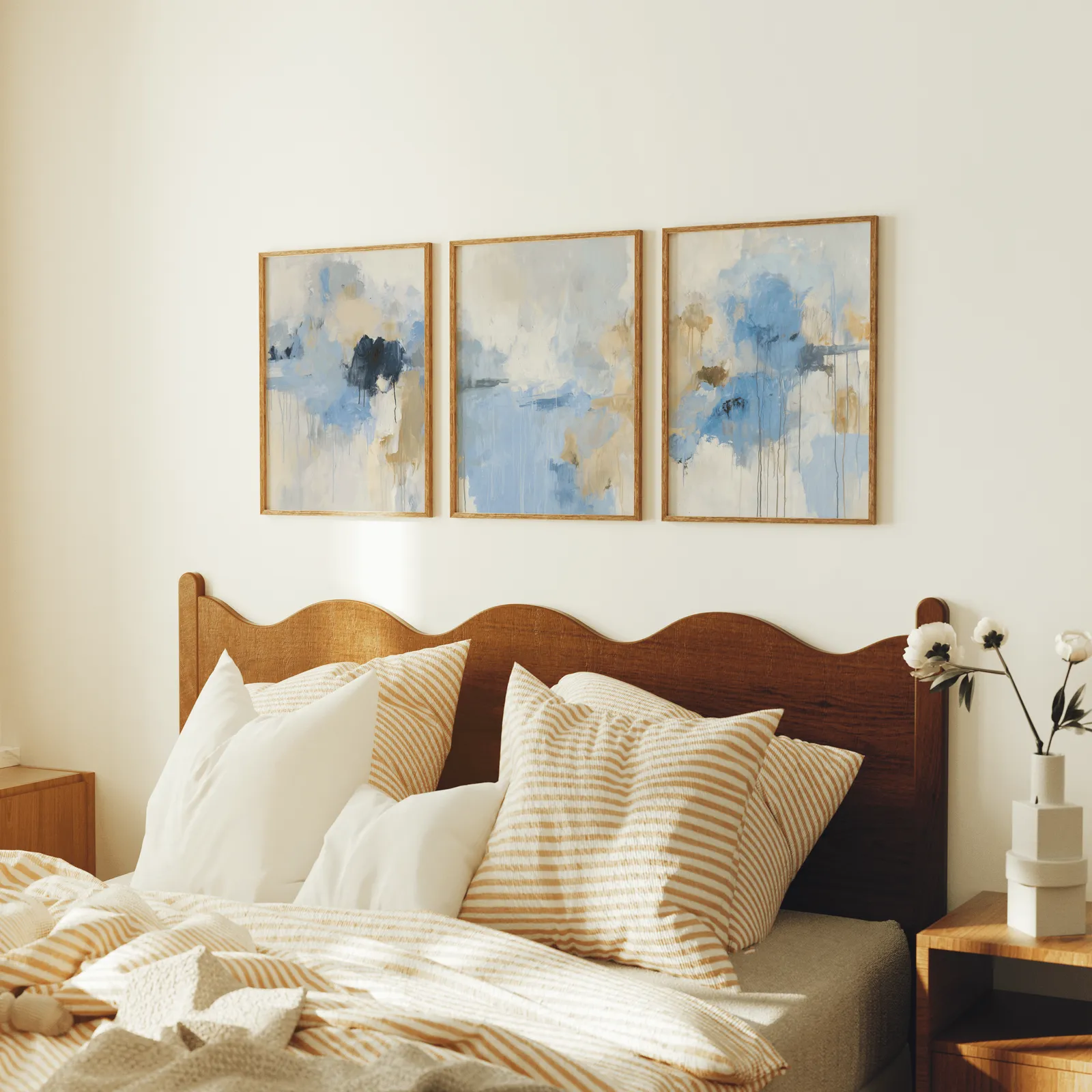 blue abstract three piece wall art, above a scalloped wooden headboard with striped pillows