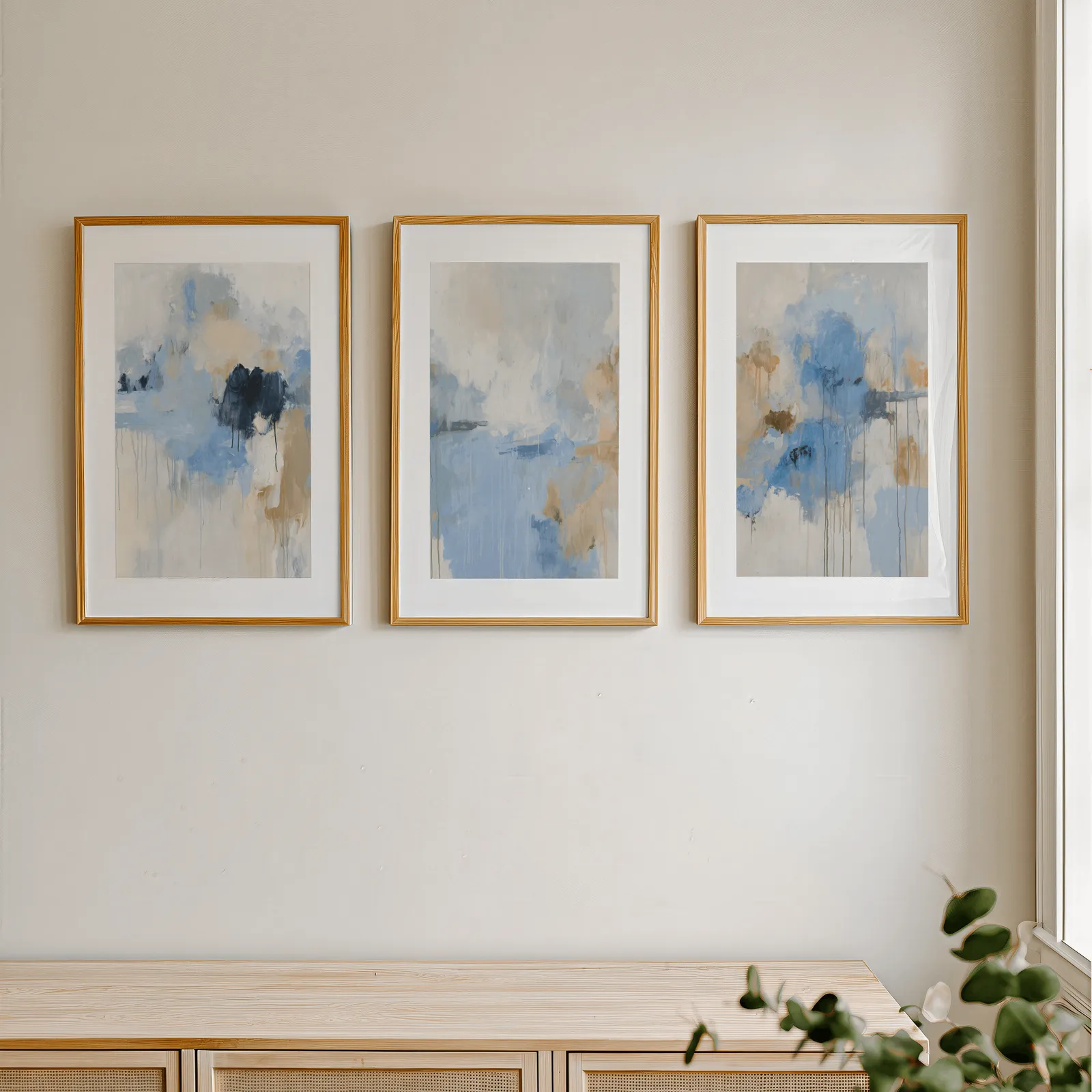 blue abstract three piece wall art, in a row above a light wooden sideboard near a window
