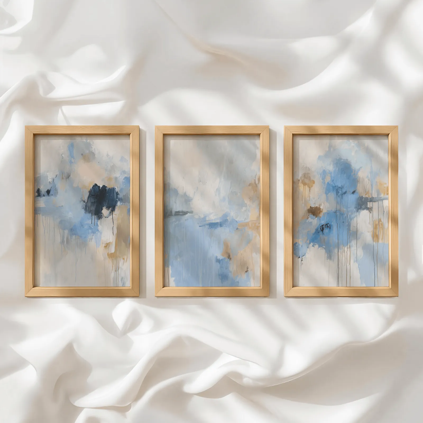 blue abstract three piece wall art, in a row atop rumpled white silky fabric