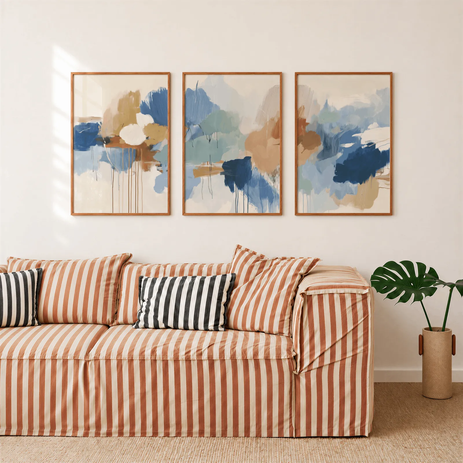 blue and terracotta abstract triptych wall art, above a rust-striped sofa beside a potted monstera