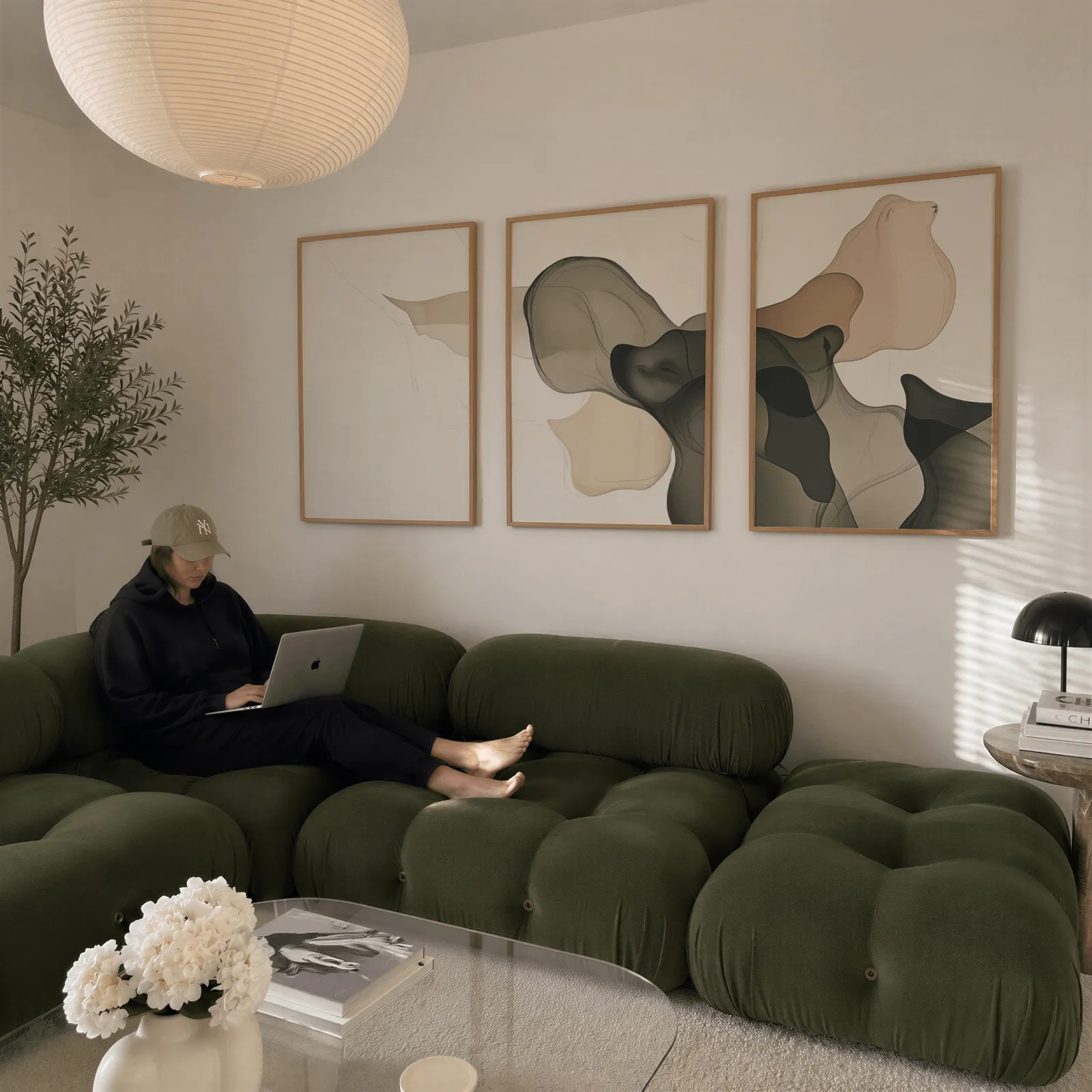 beige grey abstract set of 3 wall art, above a plush olive velvet sectional beneath a paper lantern light