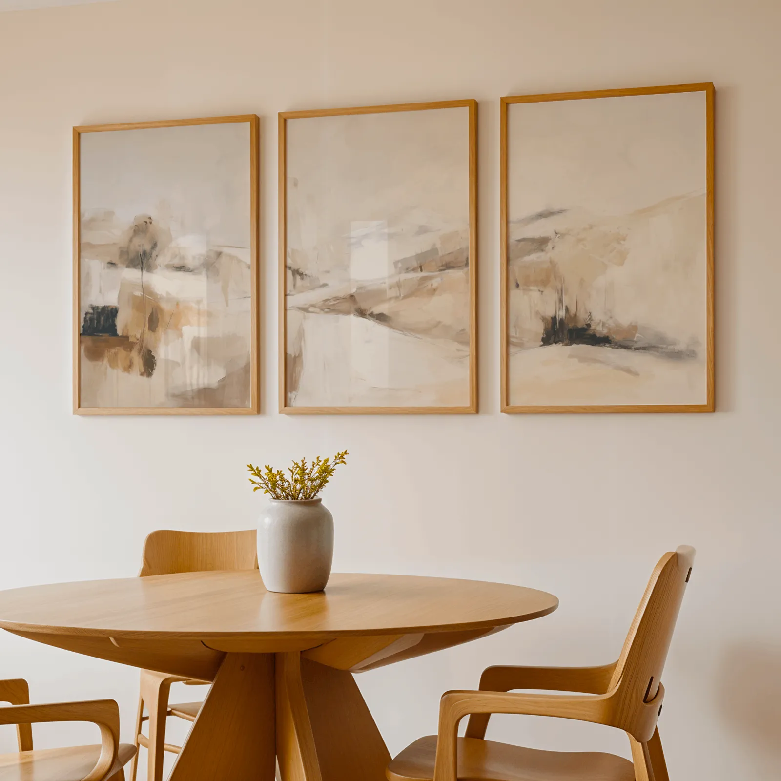 beige abstract landscape wall art set of three, above a round wooden table with a stoneware vase