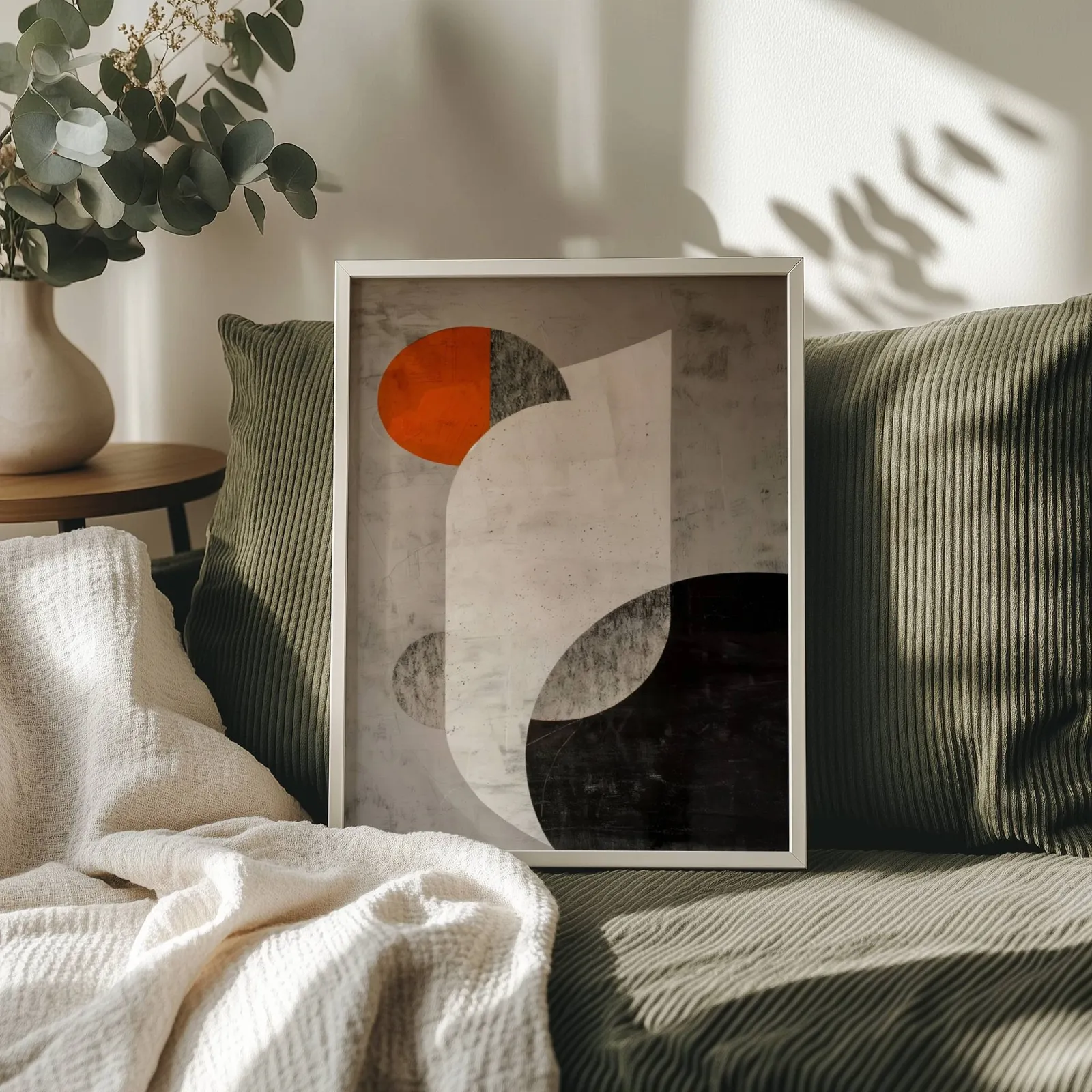 orange and black abstract geometric wall art, propped on an olive corduroy sofa beside a eucalyptus vase