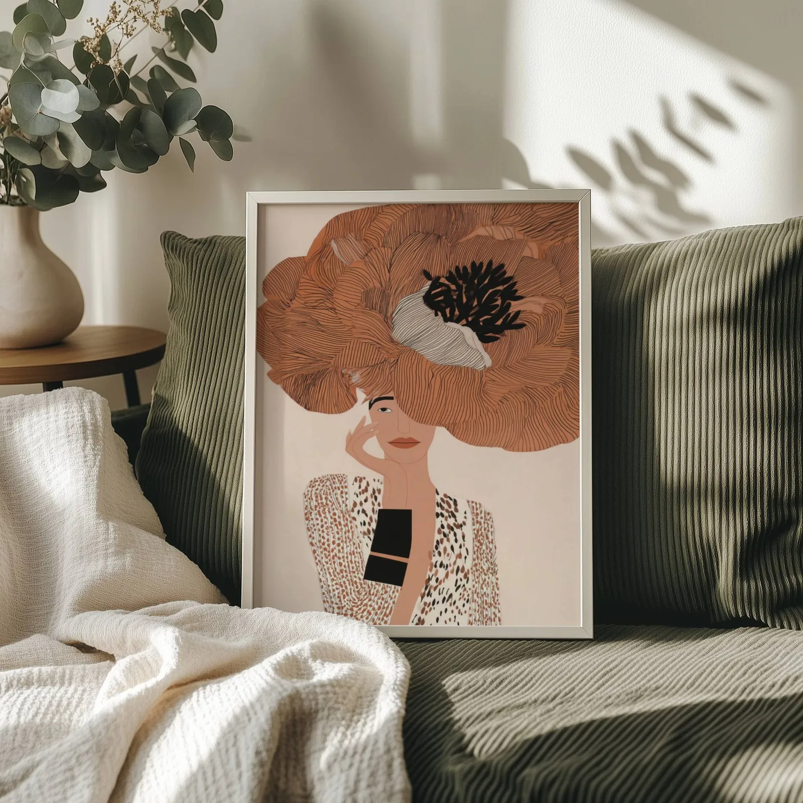 terracotta floral woman portrait wall art, propped on an olive corduroy sofa beside a eucalyptus vase