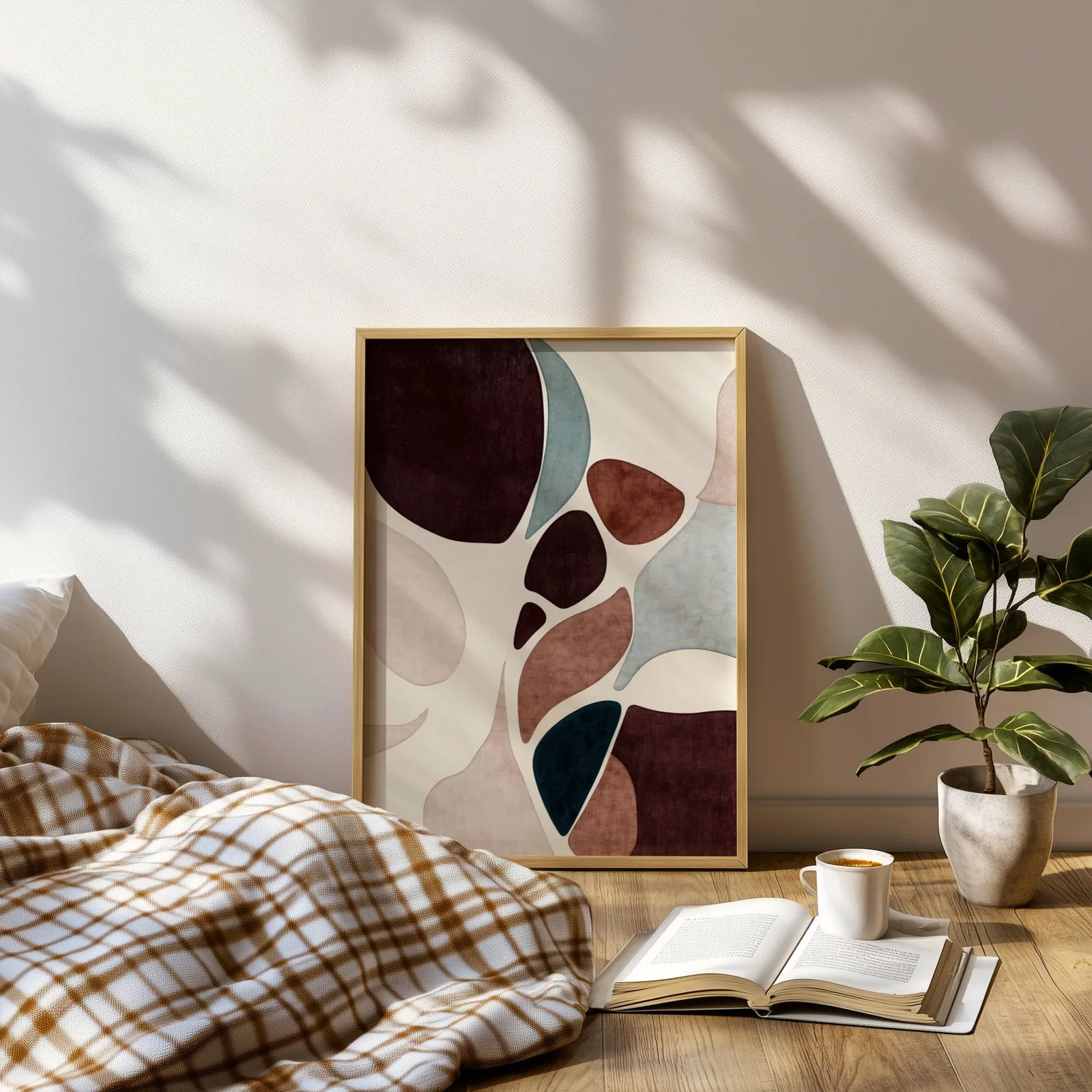 burgundy terracotta abstract organic shapes wall art, leaning on a sunlit floor beside a plaid blanket and open book