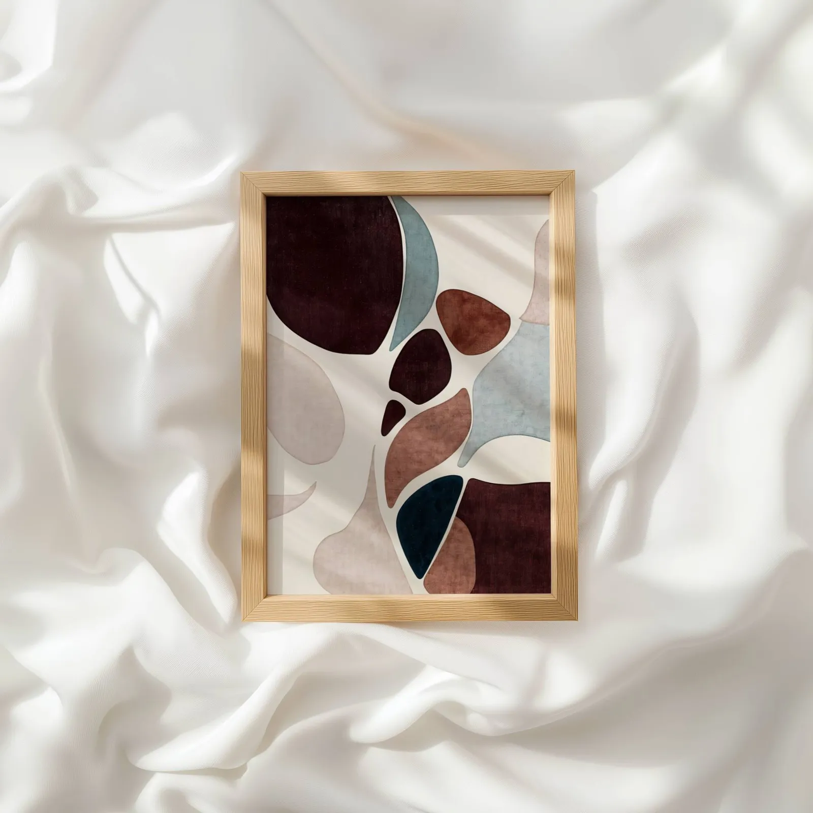 burgundy terracotta abstract organic shapes wall art, resting atop rumpled white silky fabric