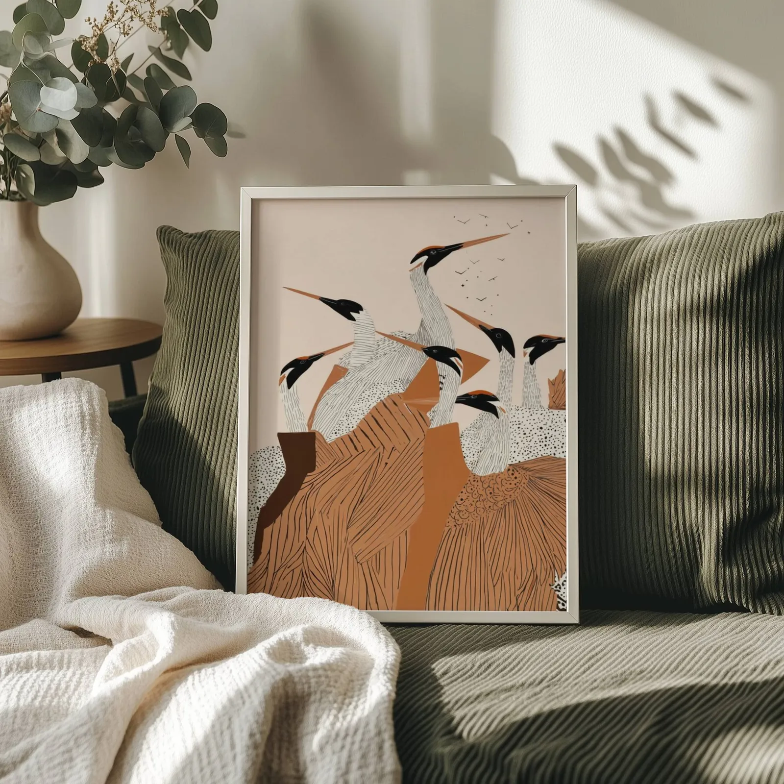 terracotta crane flock nature wall art, propped on an olive corduroy sofa beside a eucalyptus vase